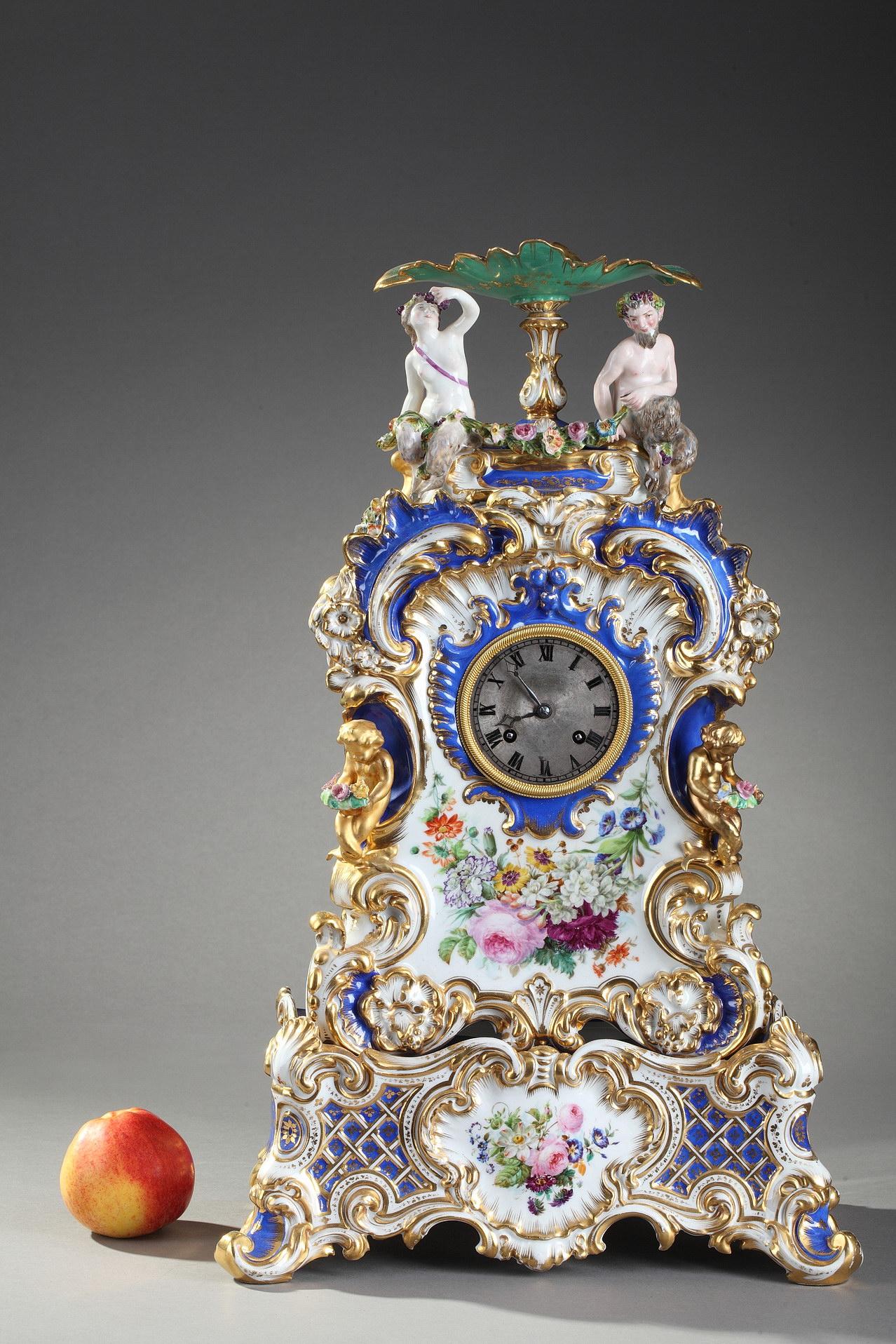 Polychrome Uhr aus feinem Porzellan, überragt von einer Bacchantin und einem Faun, der unter einer Tasse sitzt und eine Blumengirlande hält. Schimmernde Dekoration aus Blumensträußen, Ranken und Blattwerk auf blauem und weißem Hintergrund mit
