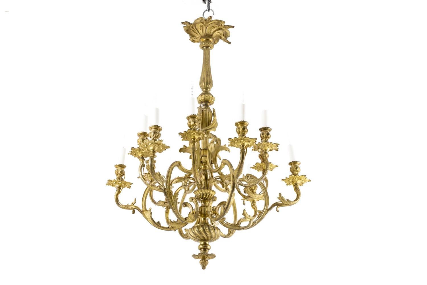 Rocaille style chandelier in gilt bronze with 12 fires. Cache-bélière (*hide hook) in rocaille rosette shape. Central shaft composed by two fluted balusters linked each other by a flat decorated with palm leaves.
Scalloped arm lights with an