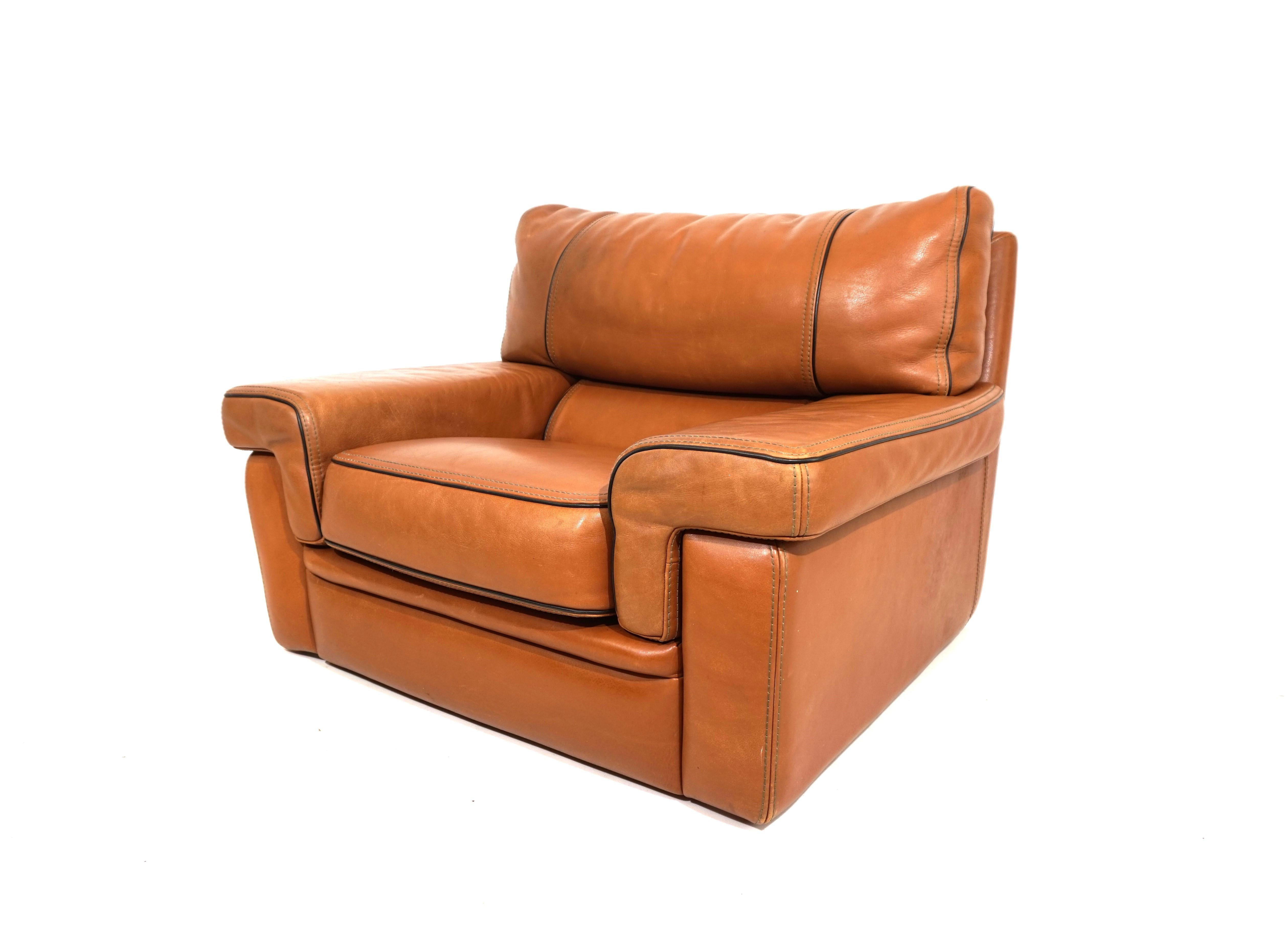 This brown, solid leather armchair made in the thick leather variant typical of Roche Bobois is in very good condition. The armchair,  in a whiskey-colored leather tone, shows minimal signs of wear, only a few stains on the back of the chair. The
