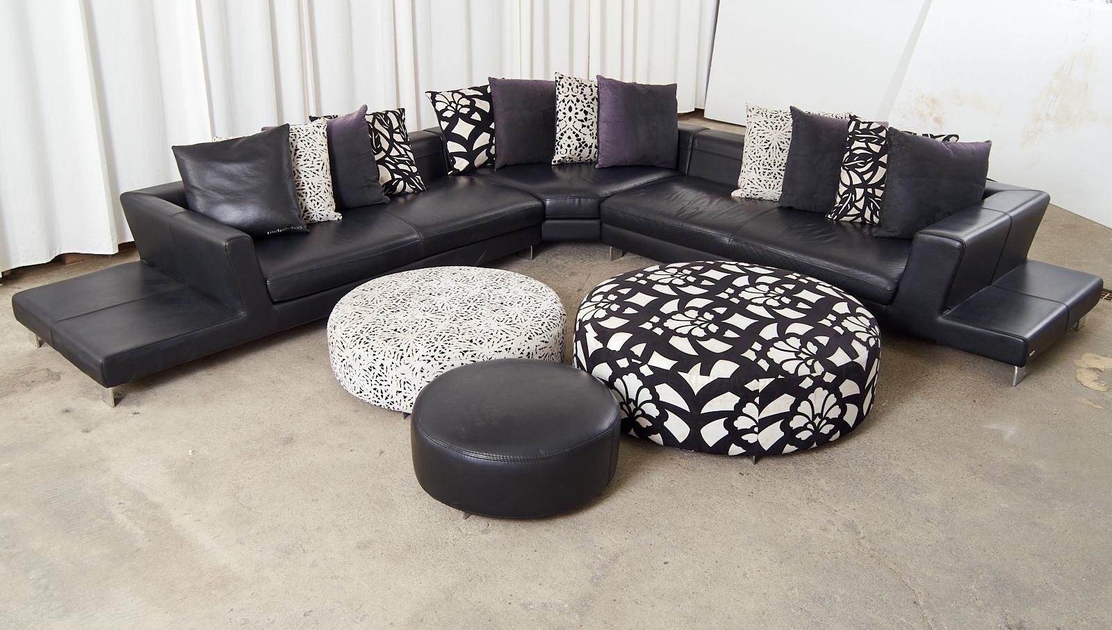 Chic black leather sectional sofa set crafted by Roche Bobois artisans in Italy. Features a monumental living room set comprised of three modular pieces and includes three round ottomans and 12 throw pillows. The large sectionals designed with