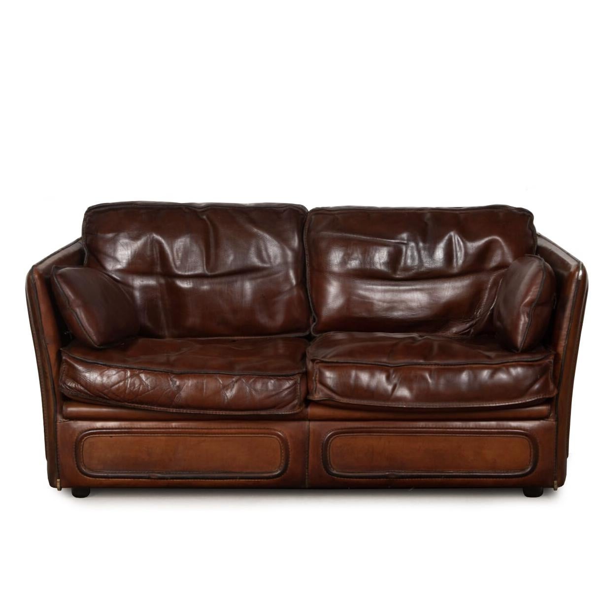 Das stilvolle Zweisitzer-Sofa aus Leder ist mit einem üppigen, dicken Sattelleder bezogen und mit abgesteppten Kanten und Metallecken versehen.

Die mit Federn gefüllten Kissen sind extrem weich und bequem.

um 1950. 

Passende Stühle sind