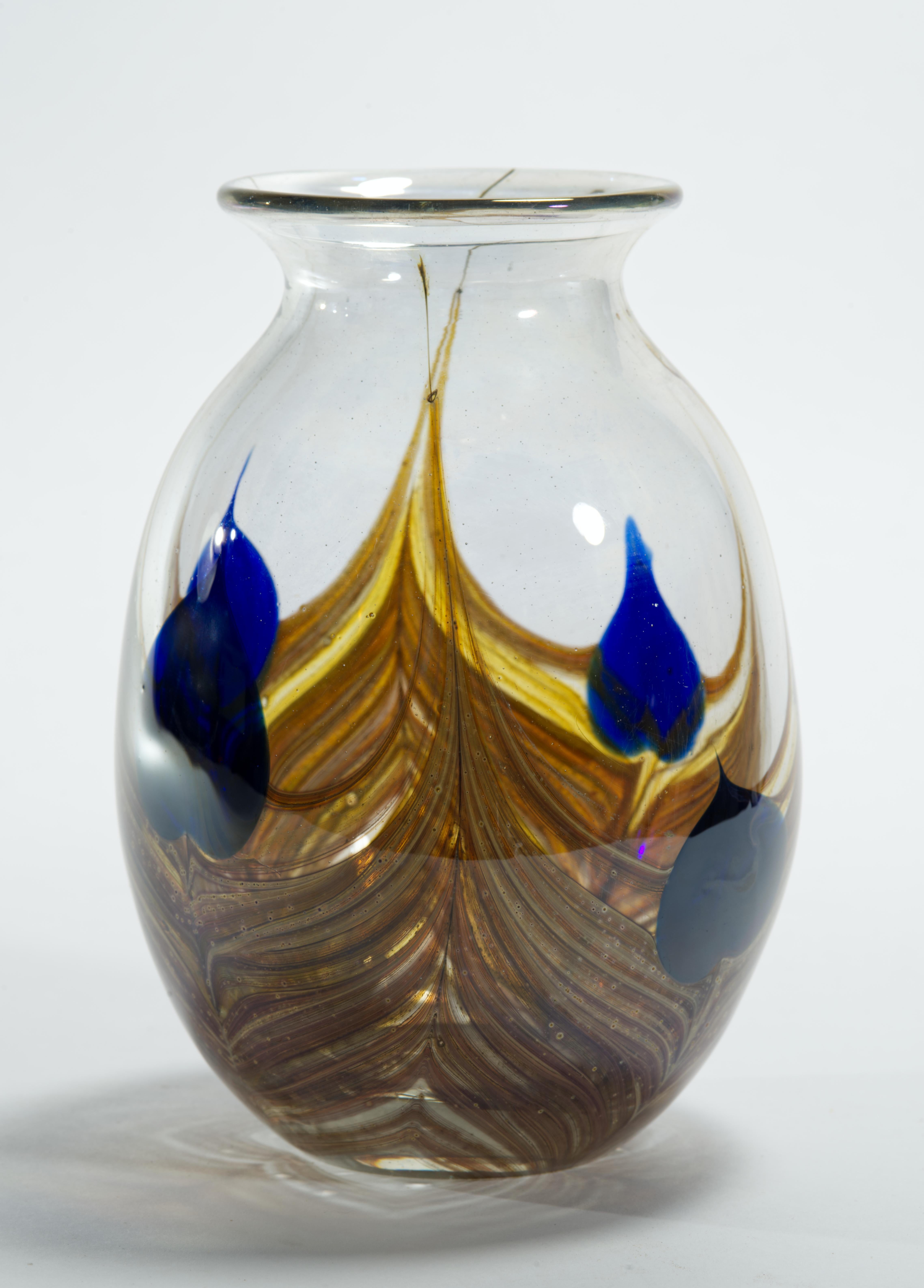 Il vaso vintage Americal Studio Glass Movement presenta il disegno di una piuma, una variante del vetro artistico degli stili Art Deco e Studio Nouveau, nei colori giallo, marrone moka e blu cobalto su sfondo trasparente.

Il vaso è firmato e datato
