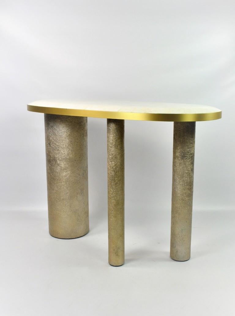 The console table Ovoid is made of a white rock crystal marquetry top.
The edges of the top are in brushed brass.
It has three cylinder legs covered made of semi raw glass fiber with a gilded patina.

The top of the console is slightly cambered