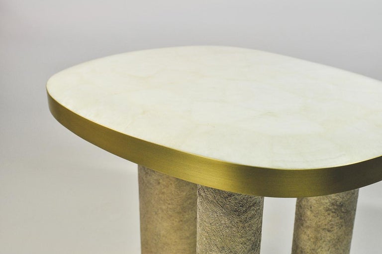 The side table Ovoid is made of a white rock crystal marquetry top.
The edges of the top are in brushed brass.
It has three cylinder legs covered made of semi raw glass fiber with a gilded patina.

The top of the console is slightly cambered on