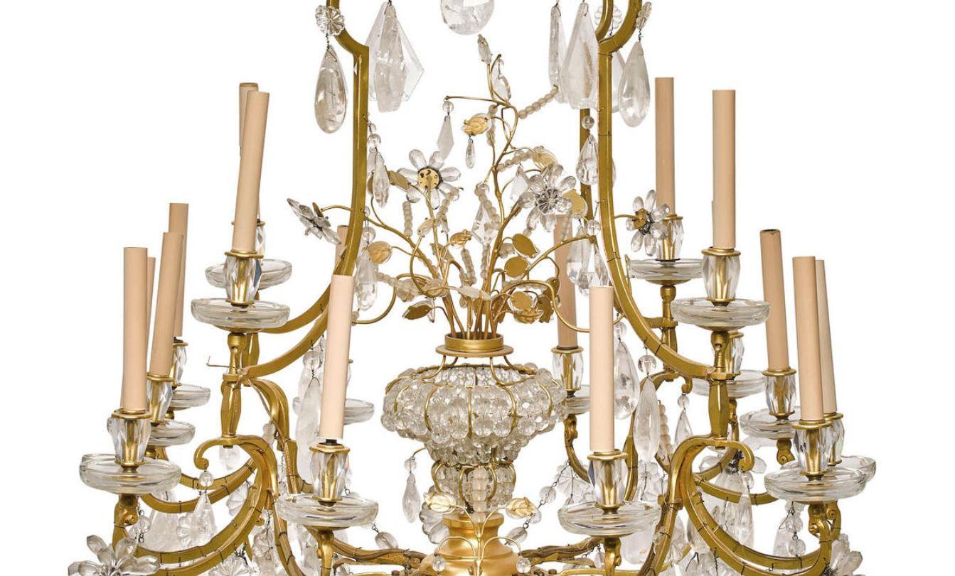 Antique outstanding neoclassical style bronze 17 light chandelier enhanced with hand carved and polished rock crystal and lead crystal prisms, rosettes, bobesches and beads. Centered with bouquet of flower in a crystal beaded vase contain one