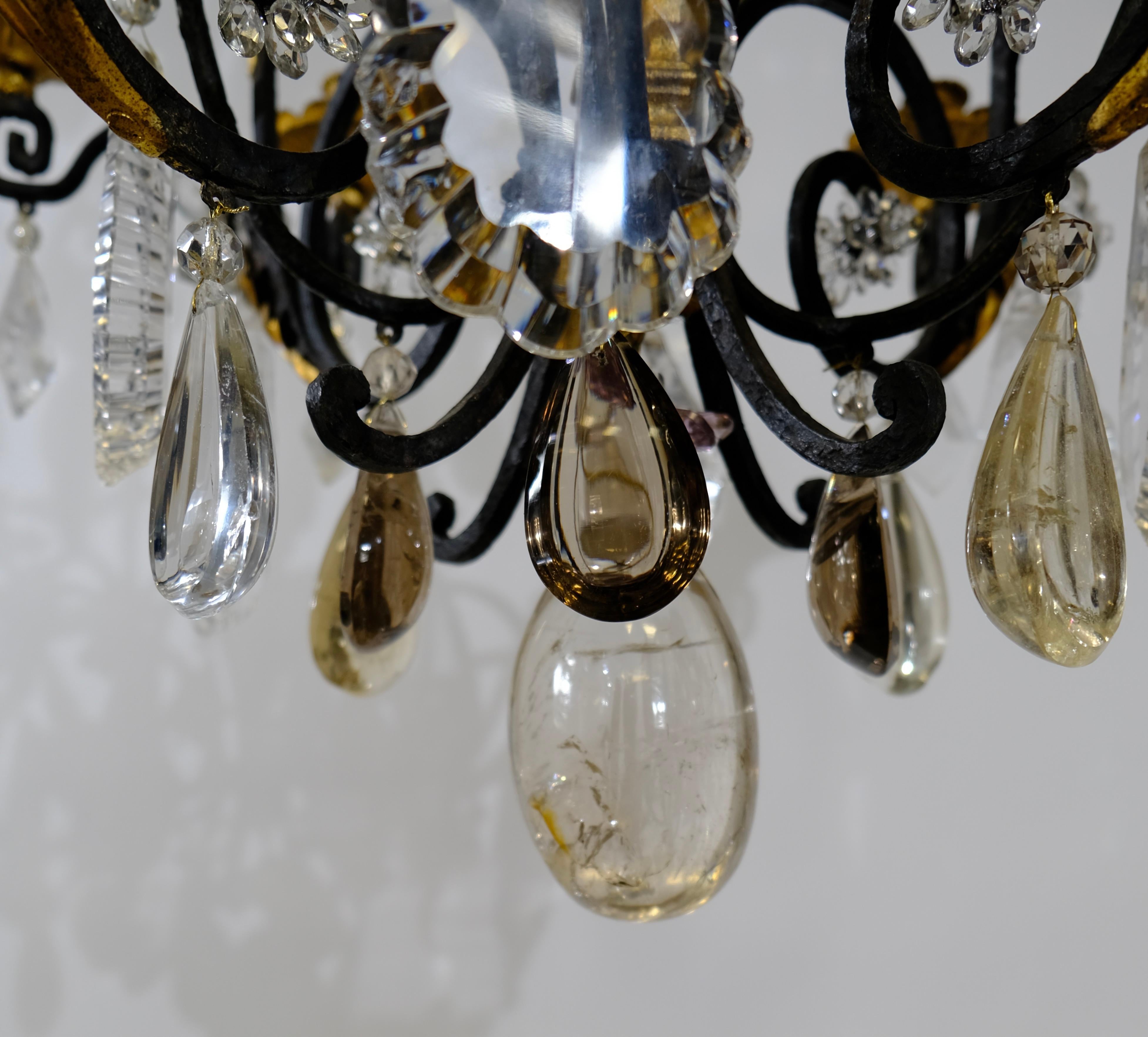 A Baroque style chandelier with 12 candleholders. The frame is forged of iron that is blackened and gilt. The chandelier is pear-shaped and has rockcrystas in the shape of leafs and fruits. Some of the pendants are made of smoky quartz.
The