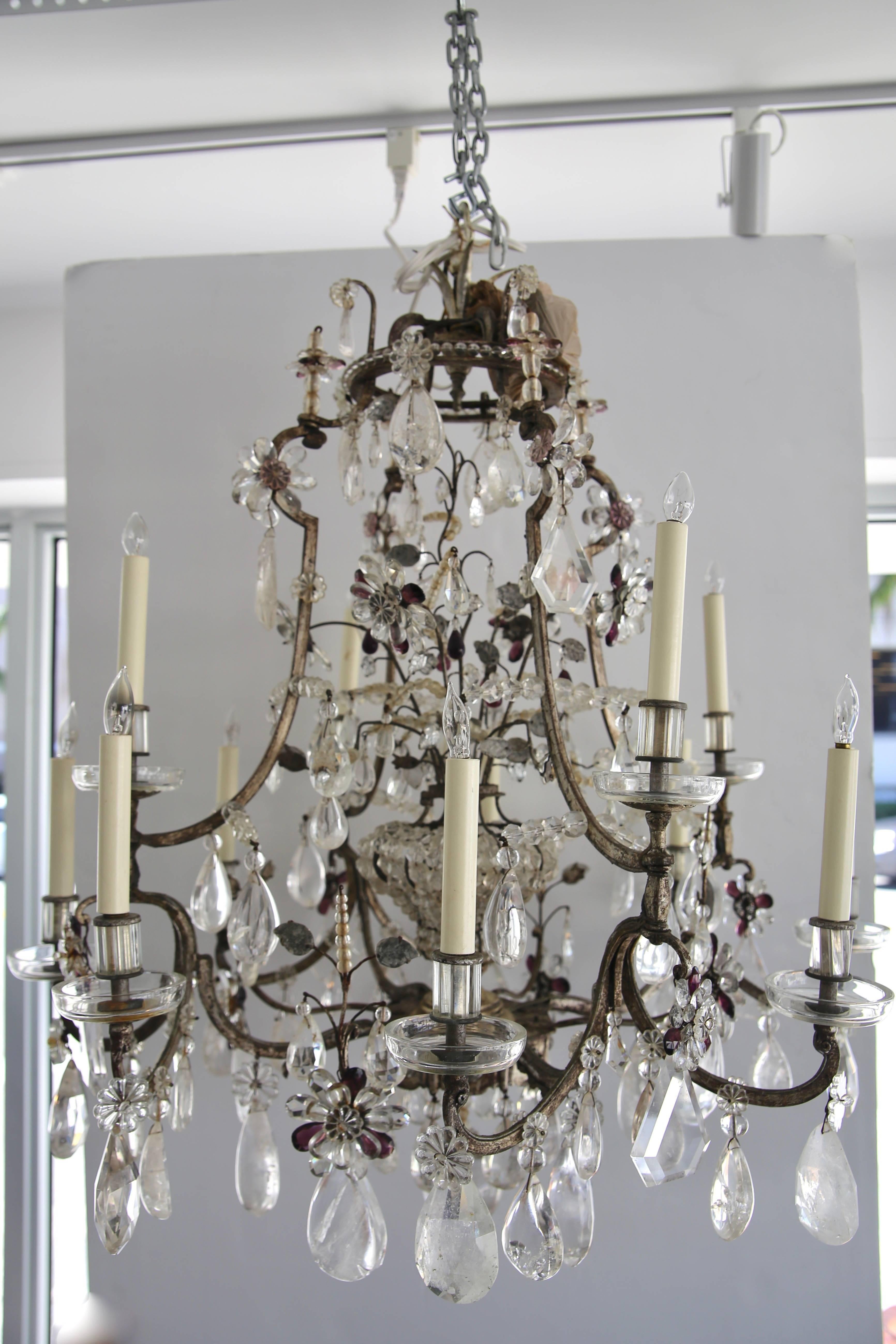 This large scale, stylish and chic rock crystal chandelier was created by the iconic firm of Maison Baguès and is in the Louis XV style with its 12 candle lights and the interior crystal cage has a single bulb. The steel frame is silver leafed and