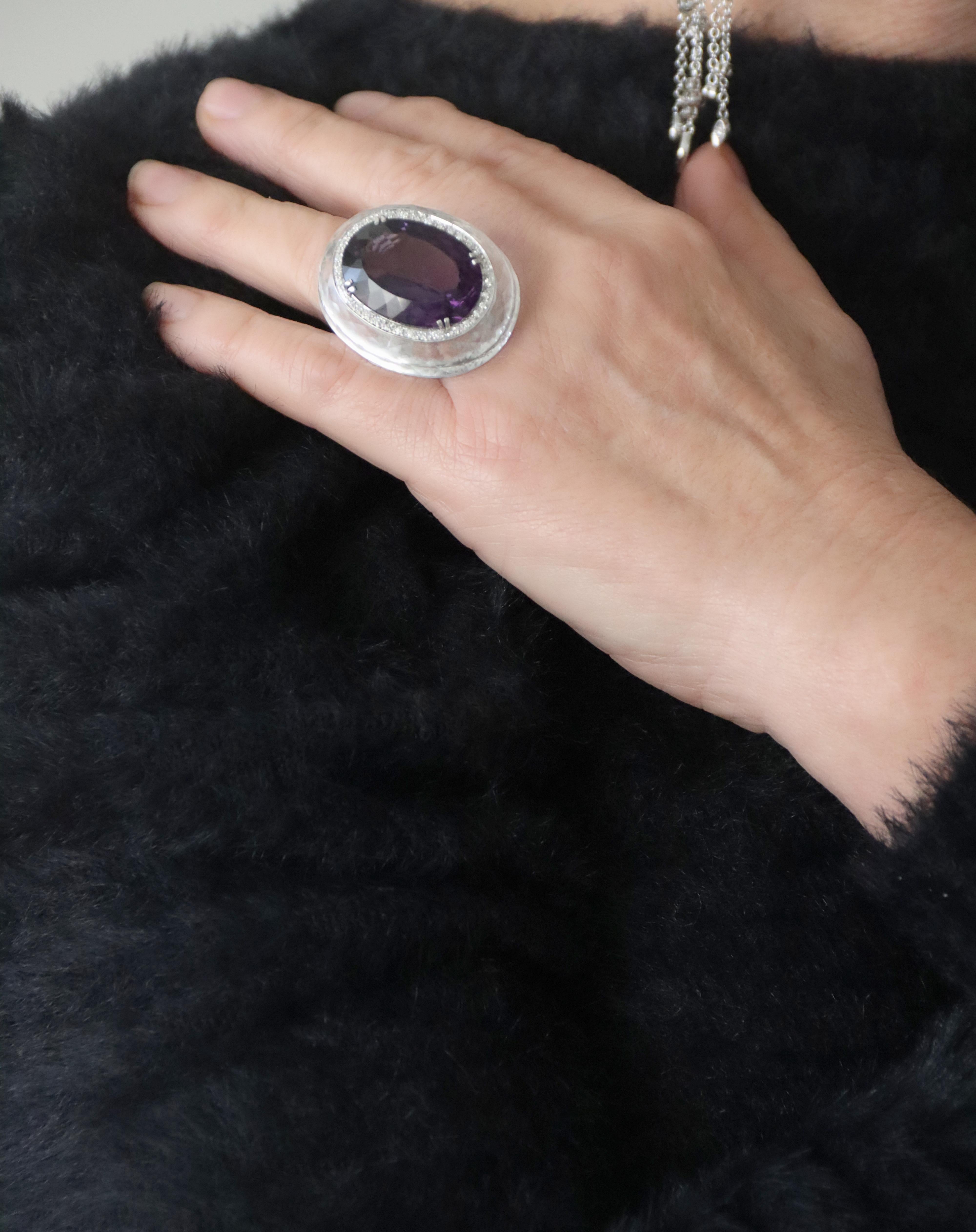 This 18-karat white gold ring is a true masterpiece of high jewelry, designed to captivate with its majestic design and choice of precious materials. At the heart of the piece lies a magnificent amethyst, featuring an oval cut that enhances the