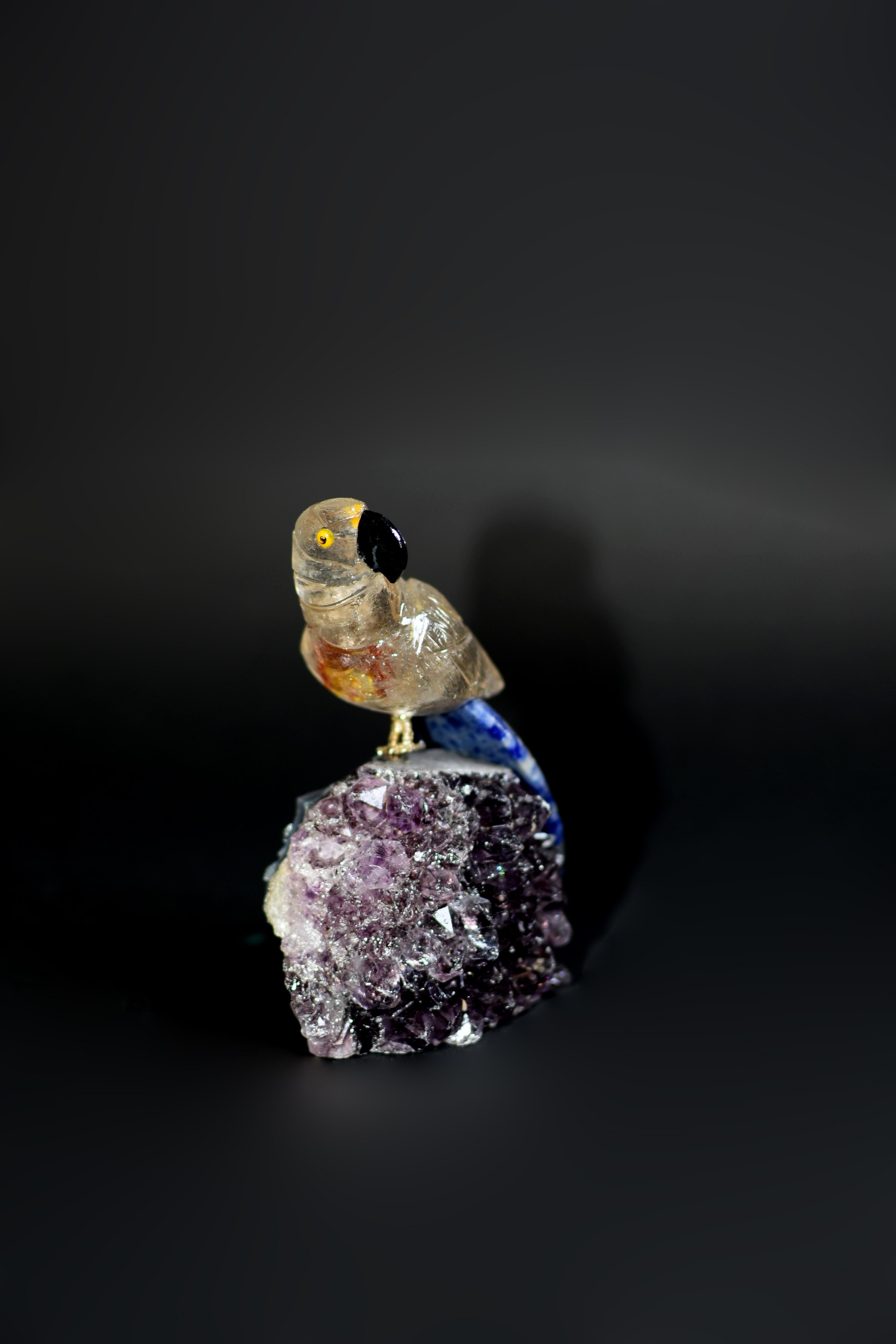 A beautiful rock crystal parrot perched on amethyst clusters. Realistically modelled with curious and amusing expression, with natural rock crystal plumage, onyx beak and sodalite tail. The rock crystal with precious, natural russet and gold