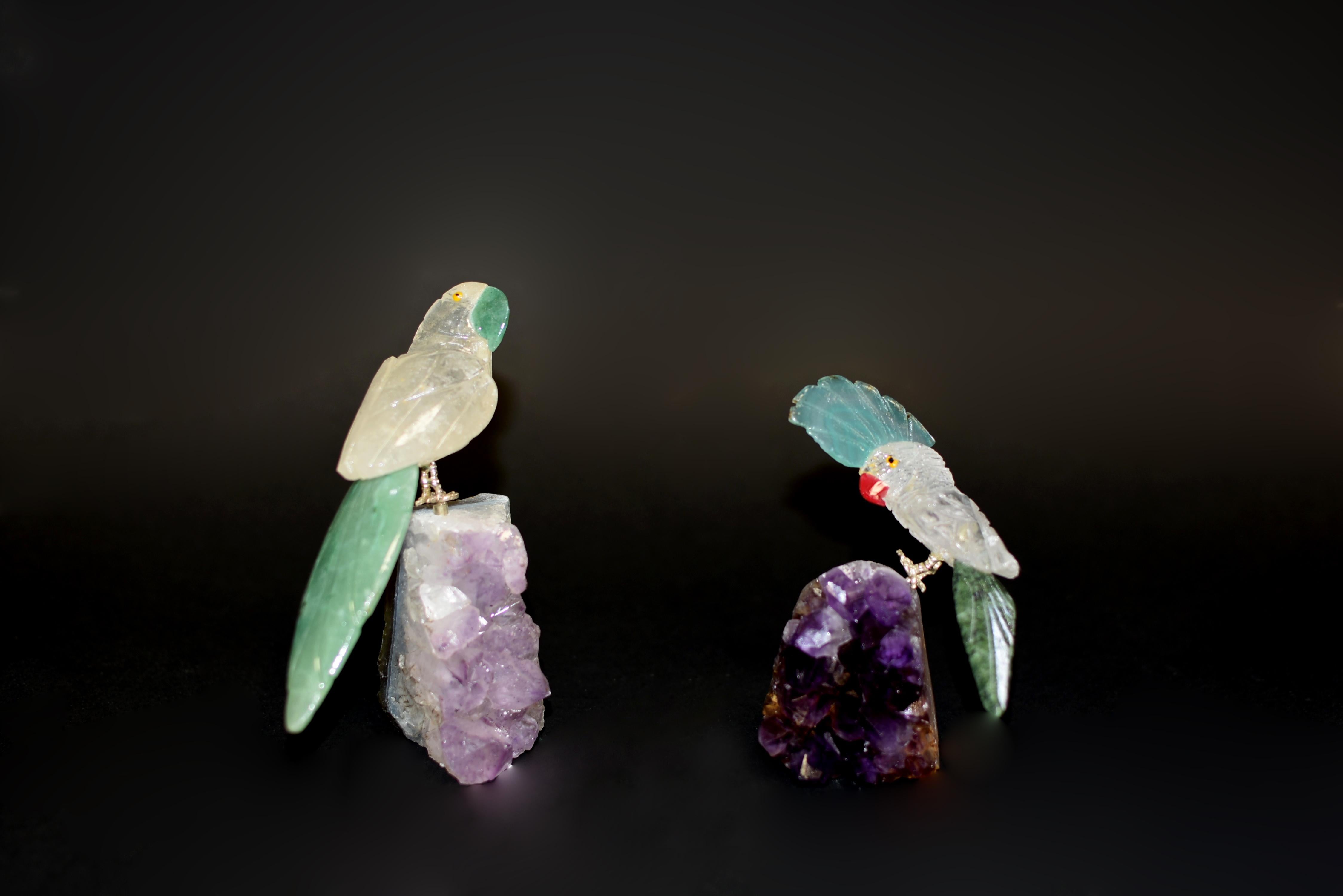 Zwei Bergkristall-Papageien, die auf Amethystbüscheln sitzen. Realistisch modelliert mit neugierigem und amüsantem Ausdruck, mit natürlichem Bergkristallgefieder, Aventurin und grünem Serpentinschwanz. Schnabel aus Aventurin und Krone aus Achat. Die