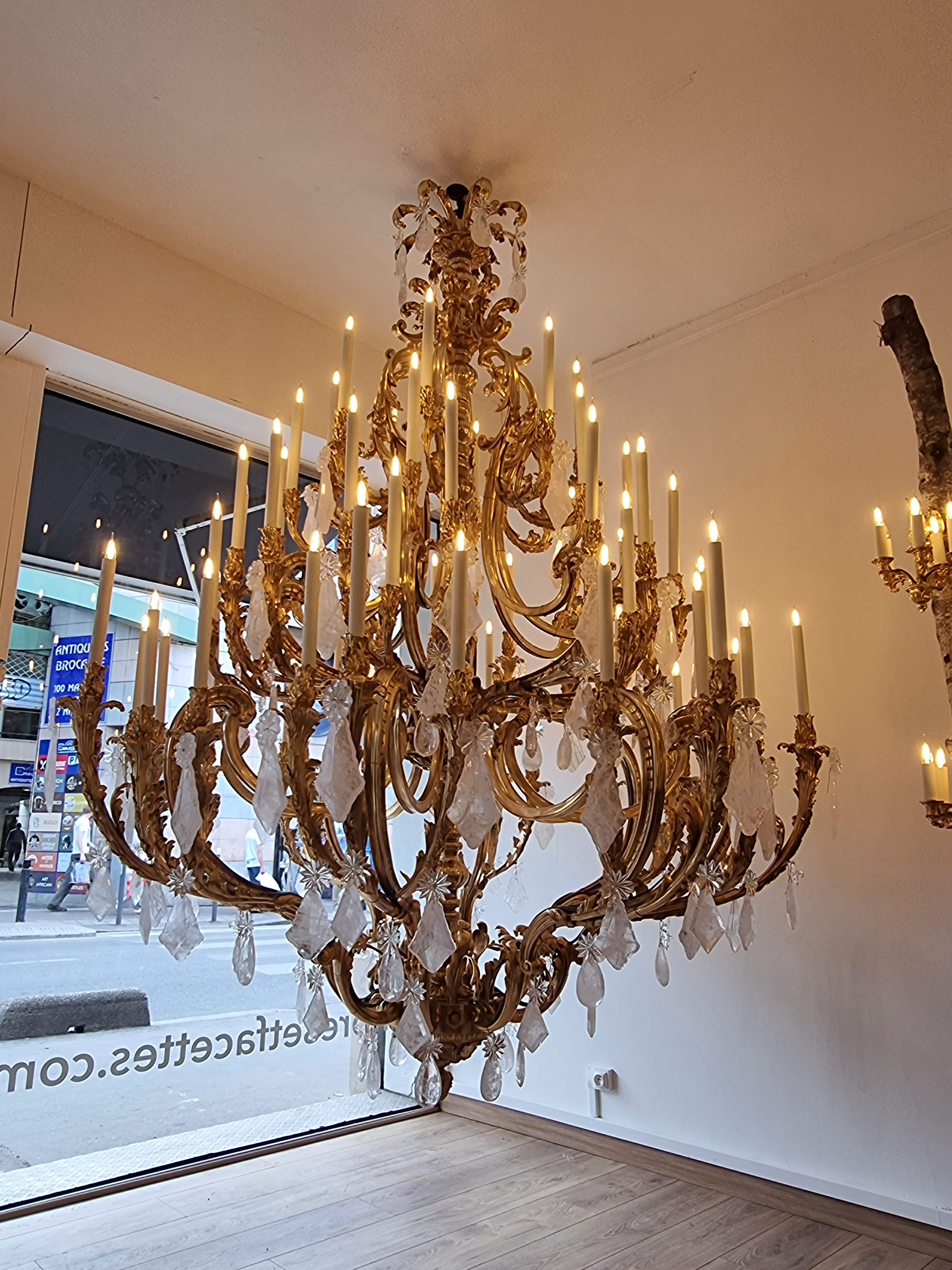 Chandelier Louis XV, In bronze, 64 arms lights, antique fuinish done on top of an  18 carats gold electrolyse.Dimensions : Height 260 cm x 190 cm diameter.

Very important Louis XV style chandelier in gilt bronze with rock crystal pendants.
Made in