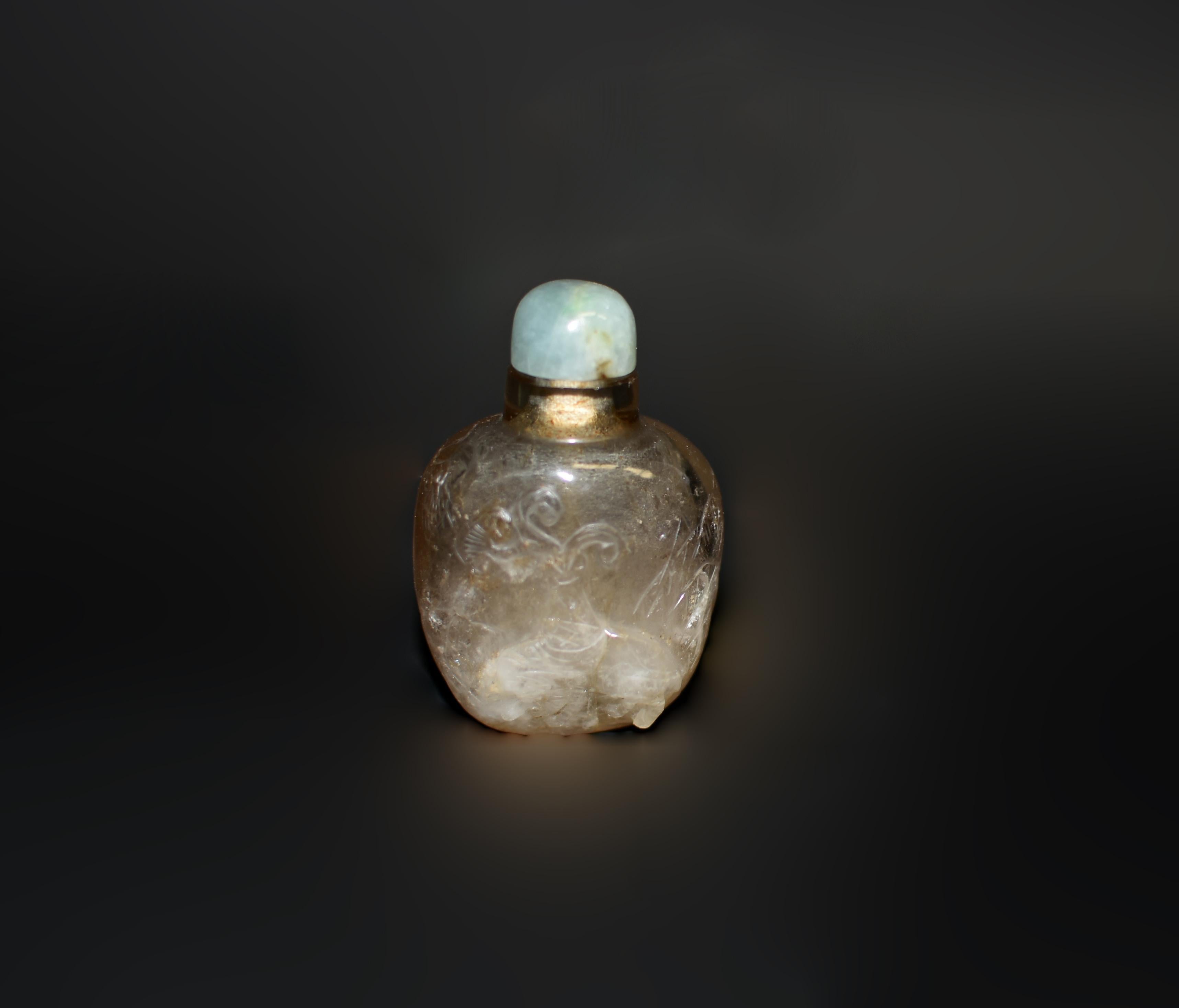 A beautiful natural rock crystal snuff bottle. Carved on the raised exterior, a vase with ruyi and evergreens atop an elephant. A large scholar's stone to the right with shoots of iris leaves. On the left a stylized butterfly above a lush banana