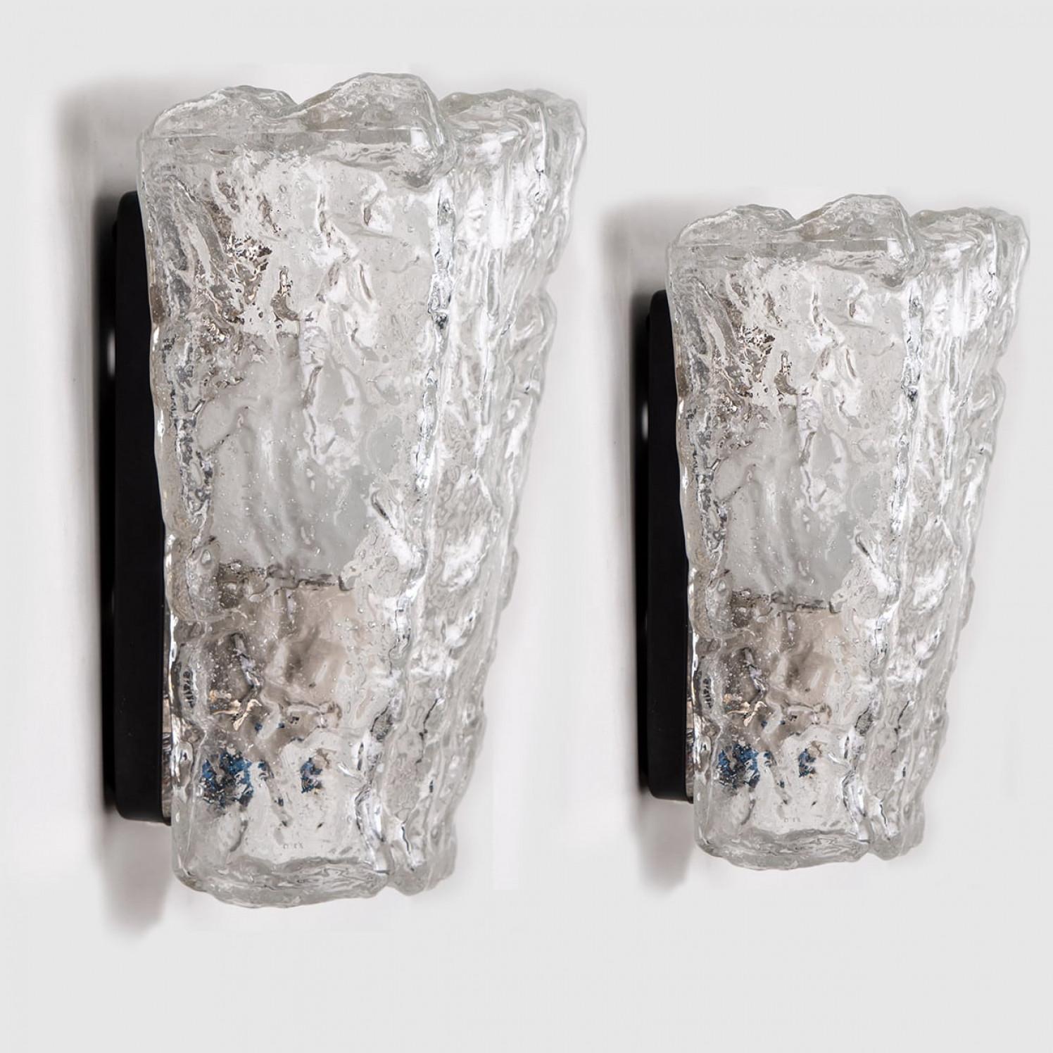 Pair of wall sconces by Hillebrand. Made in Germany around 1960.
The glass shade looks like a clear piece of rock. The glass refracts the light beautifully, filling a room with a soft glow.
The wall light features a black back plate and chrome