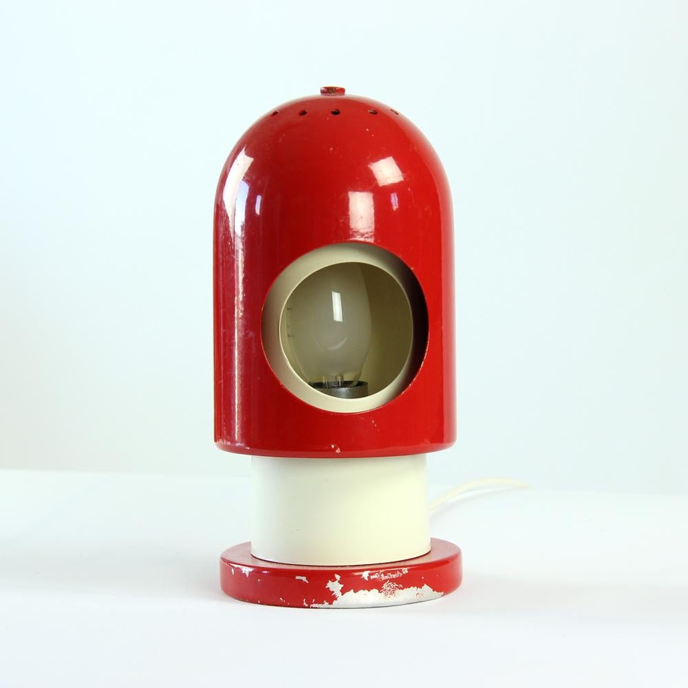 his is a great table lamp inspired by the space age era in Midcentury design period. Produced in Austria. This lamp is fully made of metal. The top part is a red shield which swivels around the cream base of the lamp which hold one bulb. This
