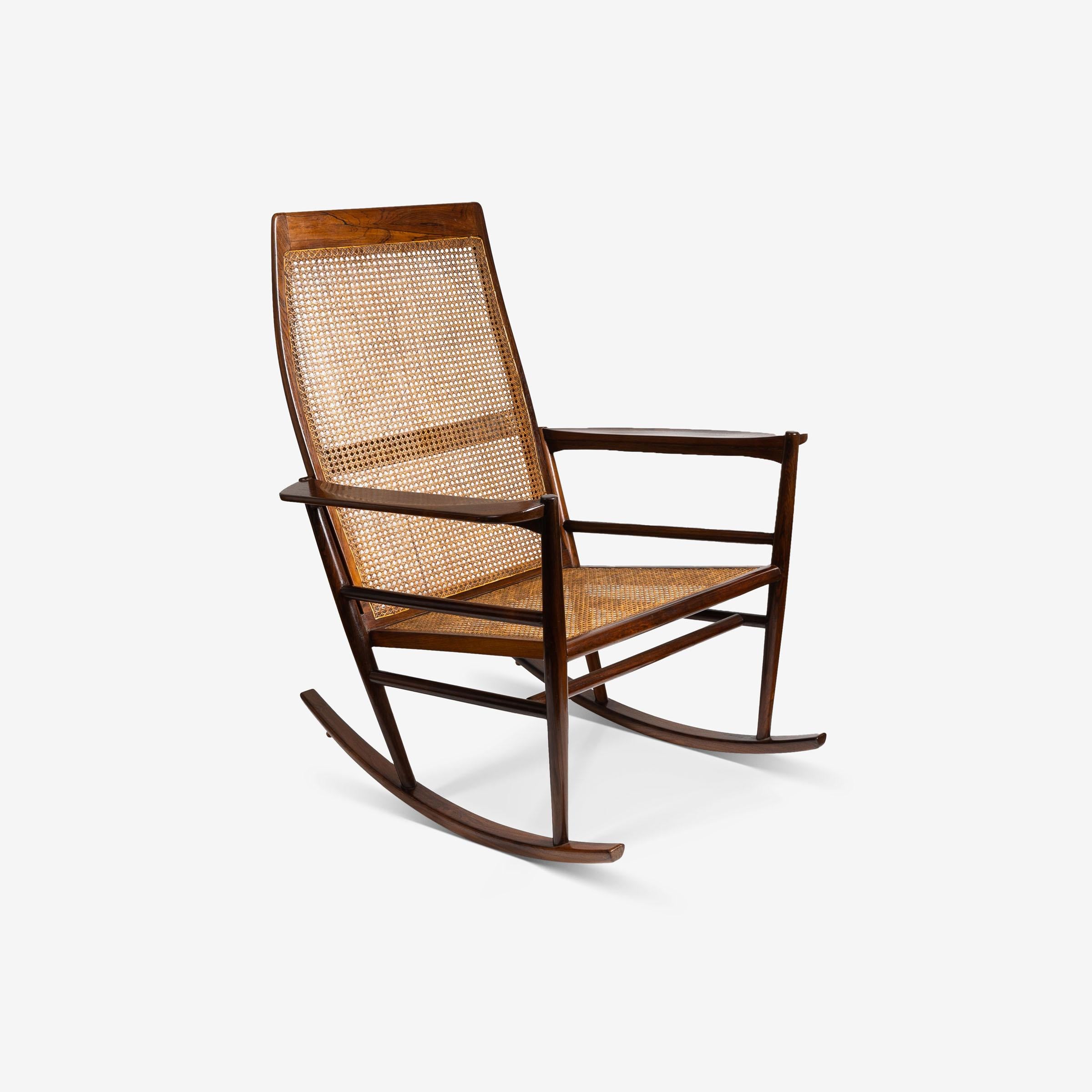 Fabriqué en palissandre jacarandá avec un cannage tressé, cet élégant rocking-chair illustre la maîtrise des proportions et de la légèreté de Joaquim Tenreiro. La géométrie raffinée et l'utilisation sobre de l'ornementation soulignent sa capacité à