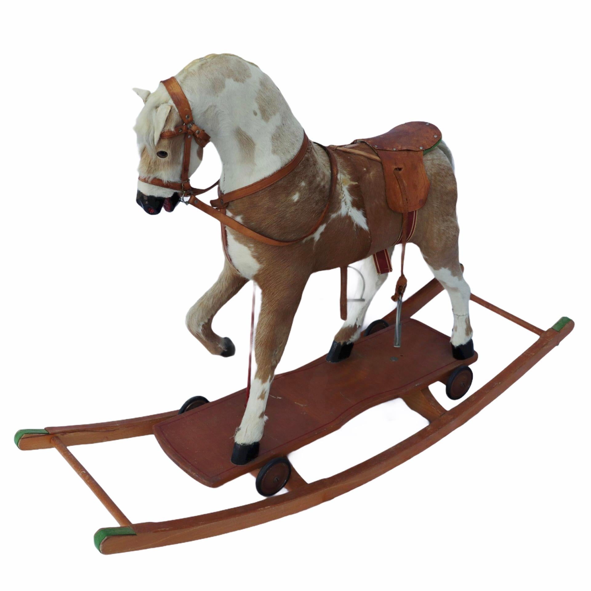 An amazing rocking horse made of wood covered in cow hide. Its saddle and reins and tack are all leather while the bit and stirrups are metal. The horse has inset glass eyes and rests wooden blades. If removed from the wooden frame, you can also use