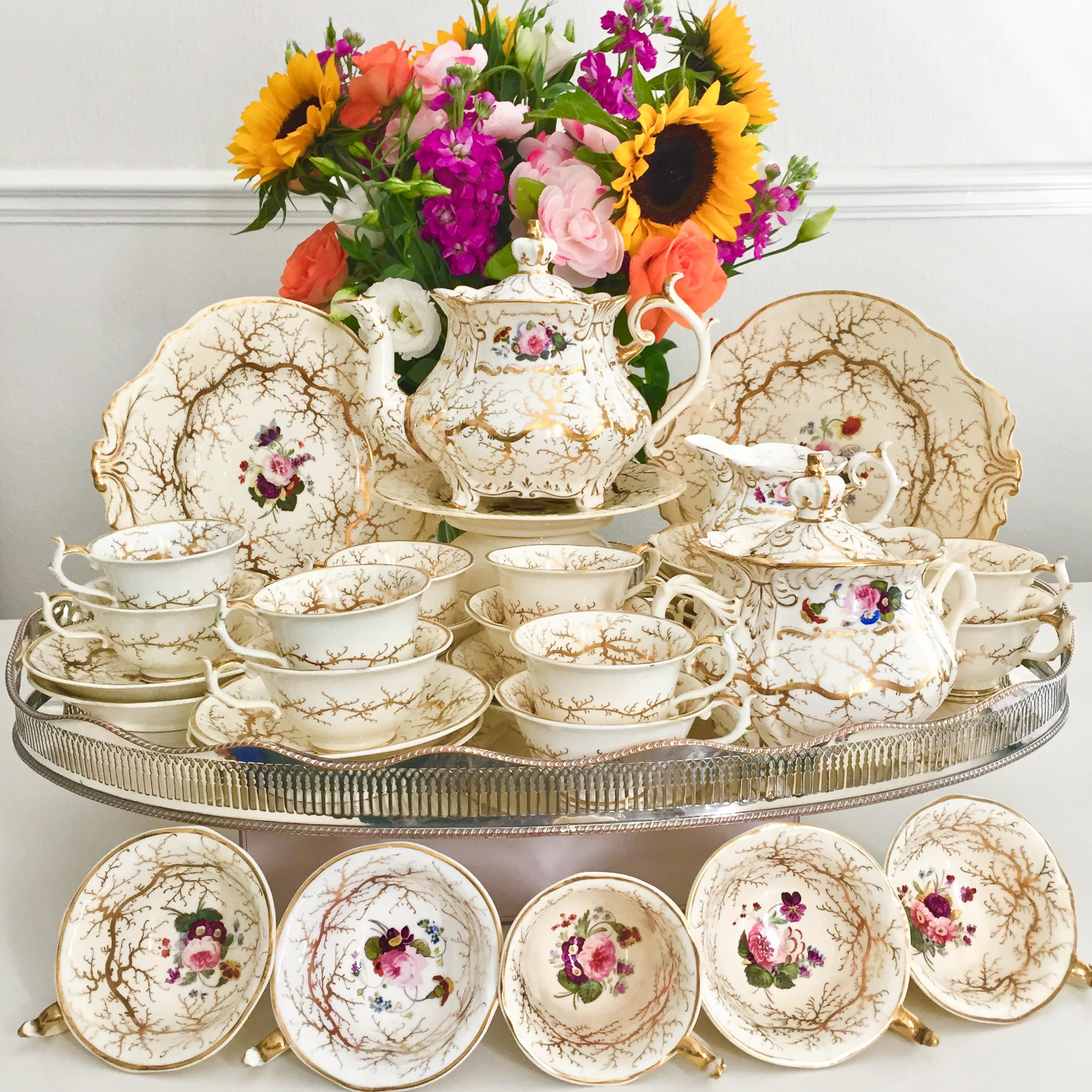 This is a stunning full tea service made by Rockingham in circa 1832, which was the Rococo Revival era. It is cream white with gilt and beautiful hand painted flowers. The service consists of a large teapot with stand, 10 teacups, 7 coffee cups, 12