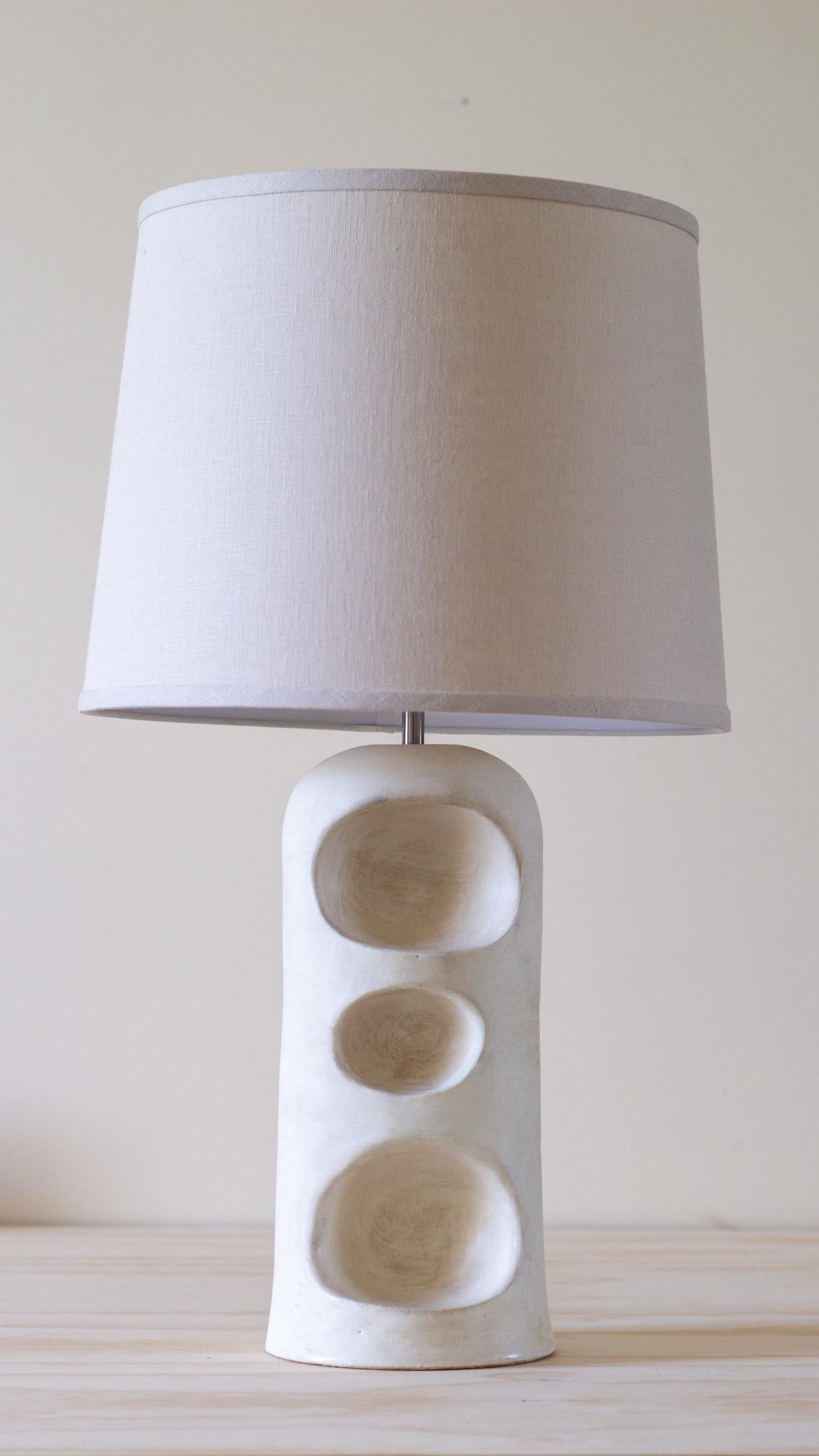Inspired by the artist’s time spent collecting stones along the coastline of Rockland, Maine, this sculptural ceramic table lamp is both a functional light source and a vessel for personal curation. Designed with three carved niches in its gently
