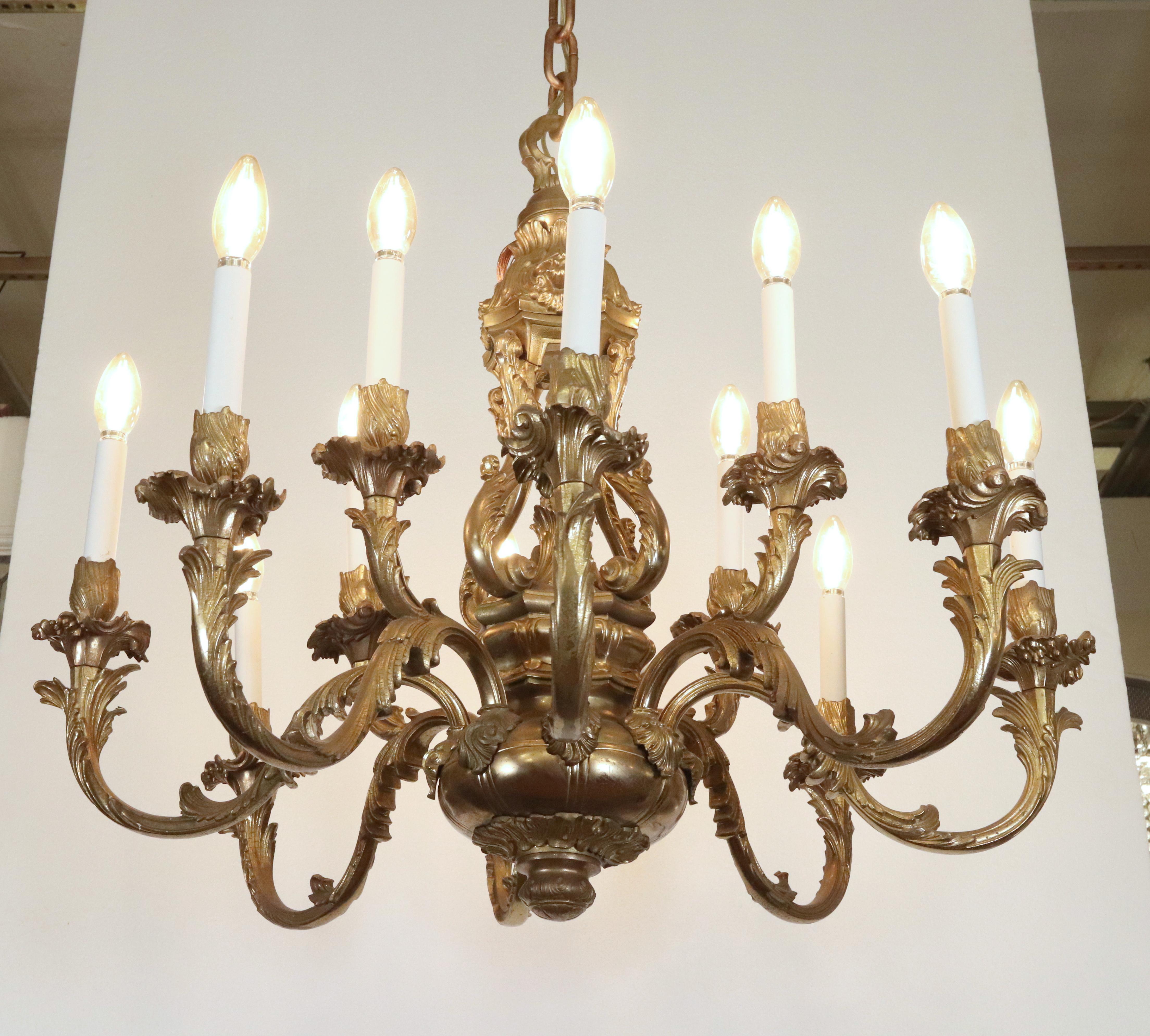 Rococo style chandelier featuring intricate scrolling arms, leaf motifs, and a highly ornate central column and canopy. It is made of solid bronze with a patina finish. This light requires twelve E-12 candelabra light bulbs. This light is cleaned