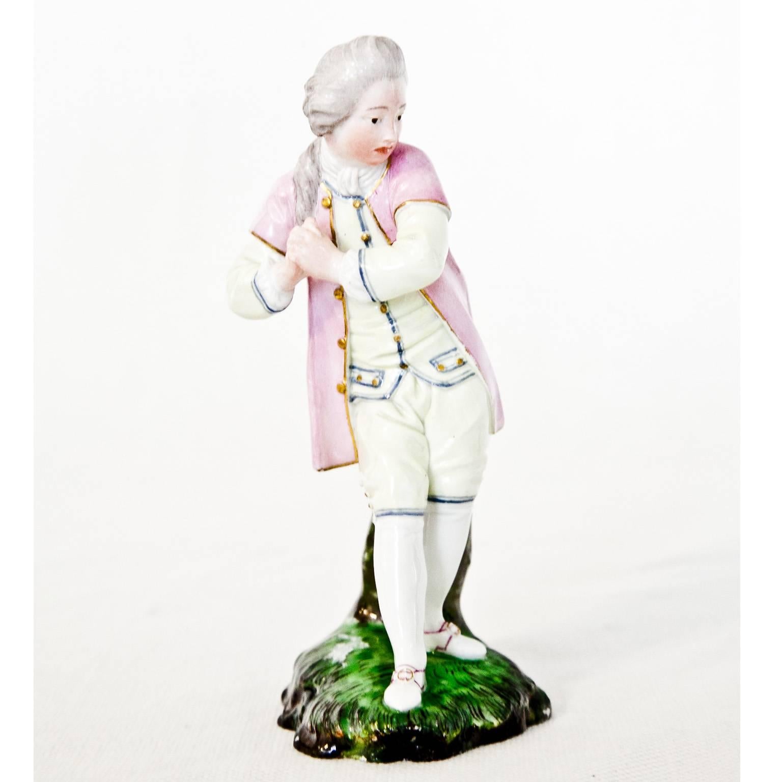 Porcelain figurine of a Rococo boy with a lamenting facial expression and posture, dressed in elegant white clothes with a rose-colored jacket. Blue mark on the bottom.