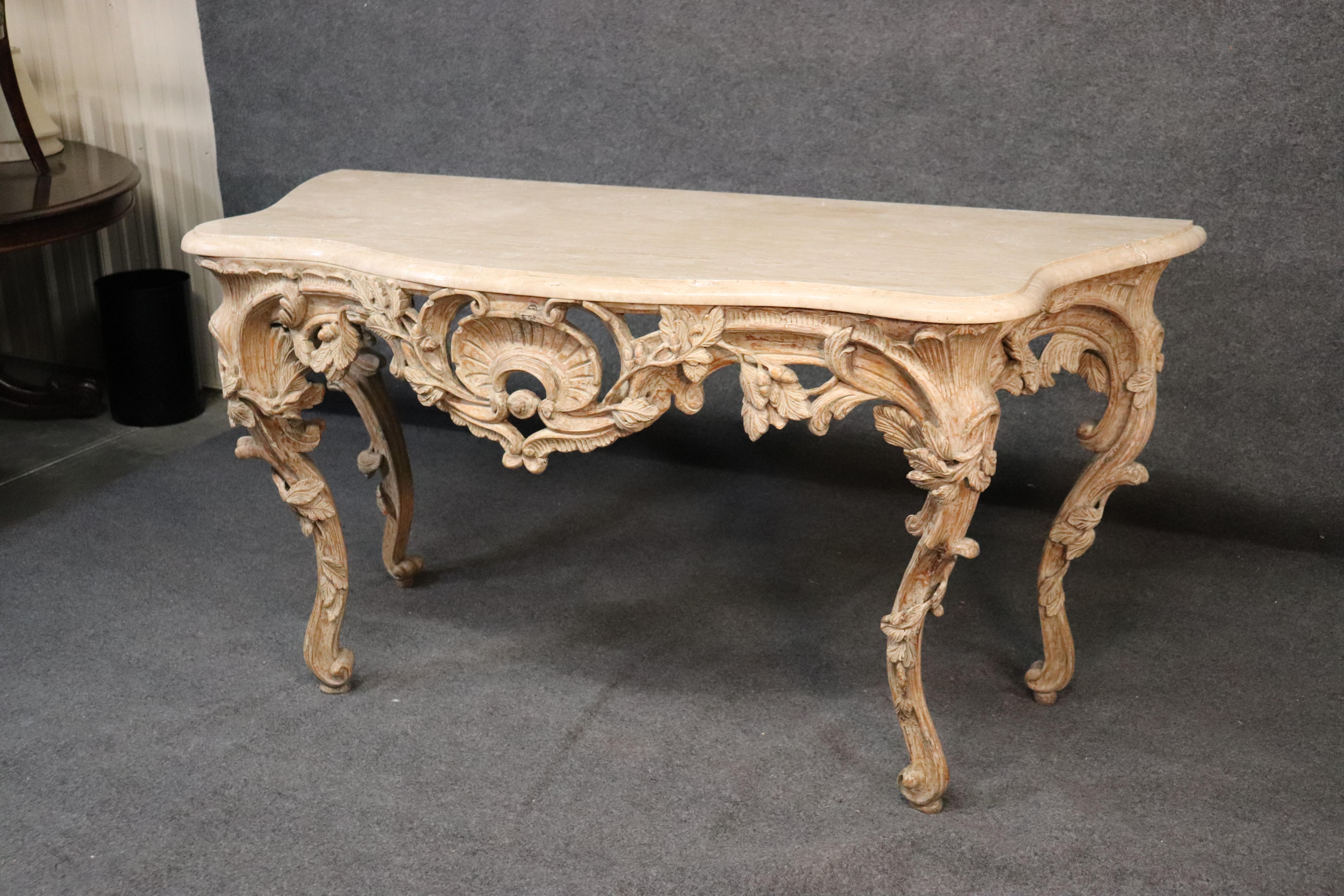 This beautiful limed finished console table has a gorgeous carved base and a beautiful white limed finish. The carving is exceptional and the travertine marble top is in excellent condition. The table measures 66 wide x 28 deep c 34 tall and dates