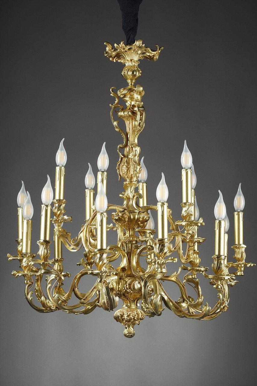Large Louis XV style chandelier in chased and gilded bronze, with nine arms of light and eighteen moving lights. The shaft of baluster form is openwork and richly decorated with rocaille, flowers and torn foliage and extends on nine arms of lights