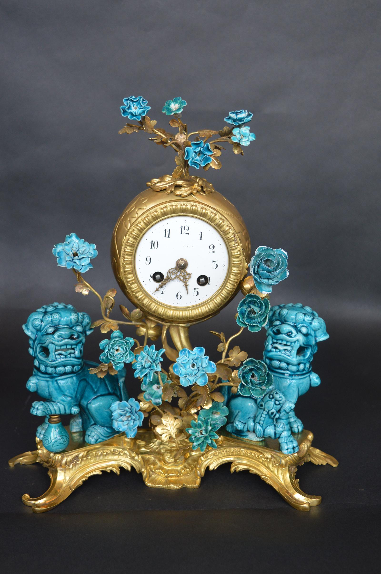A French Rococo chinoiserie style three-piece gilt bronze and porcelain clock garniture, circa 1900, comprising a gilt bronze mantel (fireplace) clock surmounted with turquoise glazed floral blossoms on gilt bronze wire stems over a cylindrical
