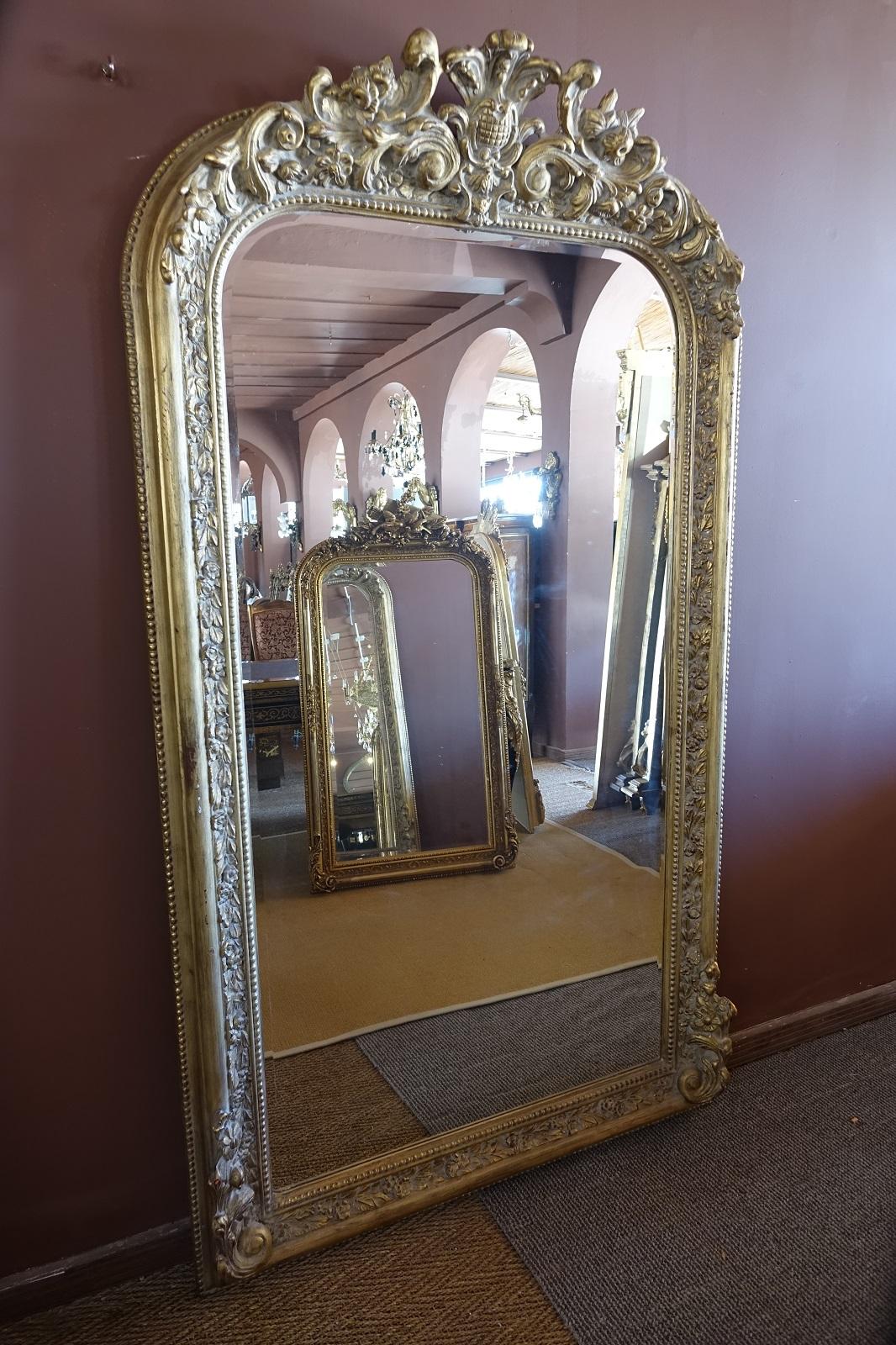 A large beveled mirror, in perfect condition and ornate gilding. Has a flat footprint and therefore can be hung elevated on a wall or flush with the floor. The subtle gilding means the piece is at home in a modern or an antique setting.