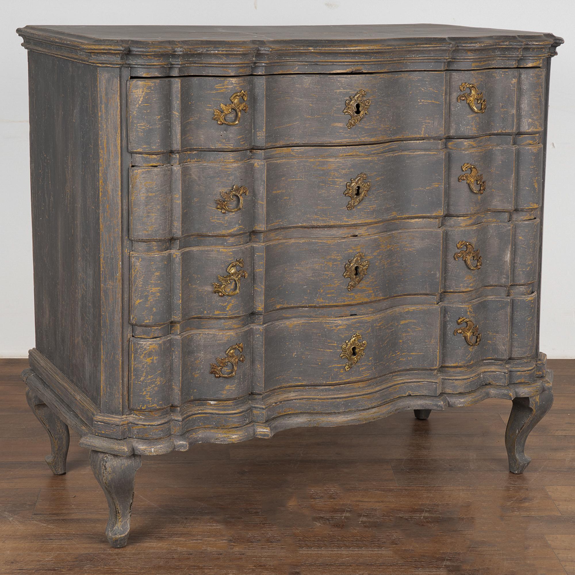 This antique rococo large oak chest of drawers features a serpentine front, brass hardware pulls and is raised on lovely cabriolet feet. 
The newer, professionally applied and layered gray painted finish is gently scraped and distressed, revealing