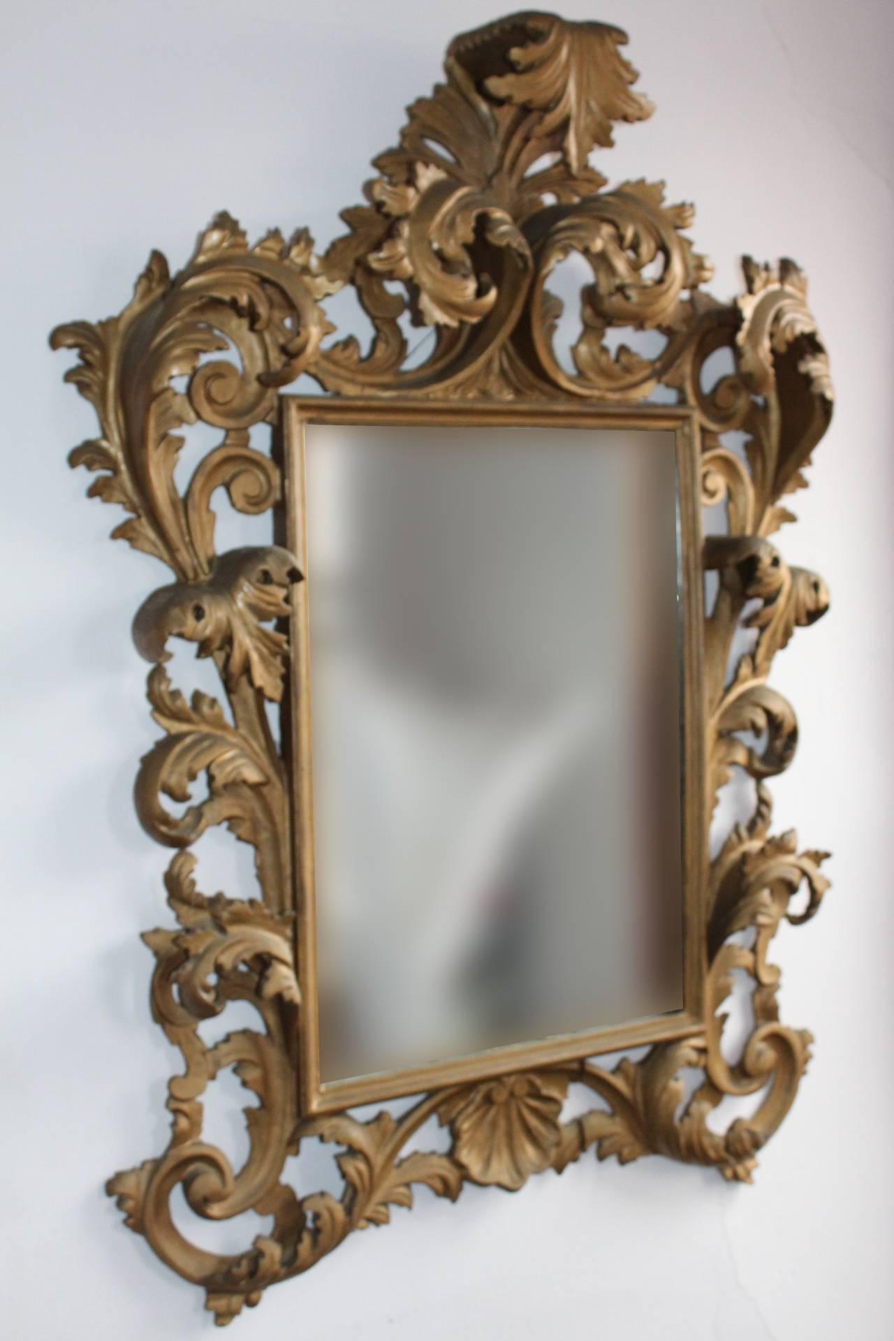Antique Italian Rococo mirror in carved wood and painted in a gold-tone with scrolling acanthus leaves. This mirror is an antique and has visible signs of age. There is a small label on the verso that states 