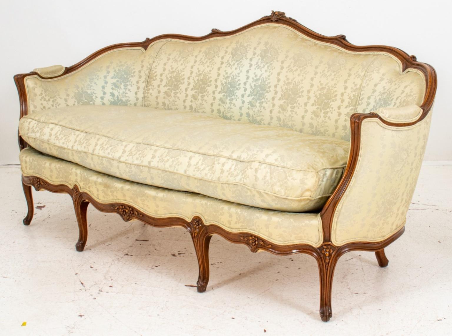 French Louis XV Rococo style sofa or settee, the fruitwood scrolling back rest with floral carvings, downswept arms and shaped seat with one above cabriole legs, upholstered in beige silky damask.

Dimensions: 34.5
