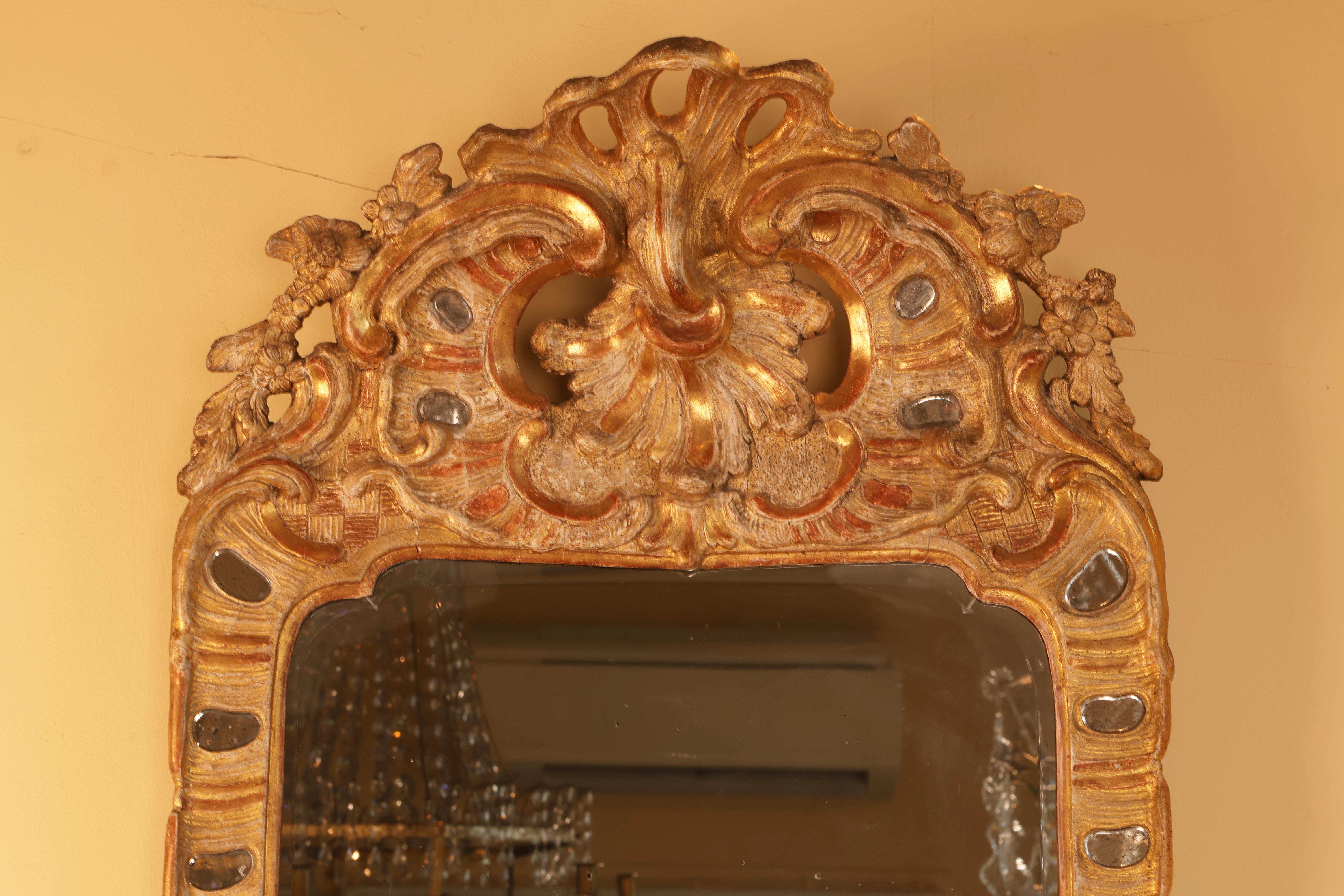 A gilded and bronzed Rococo mirror with lenses from the 18th century. The mirror features a richly ornamented crest adorned with rocaille motifs.