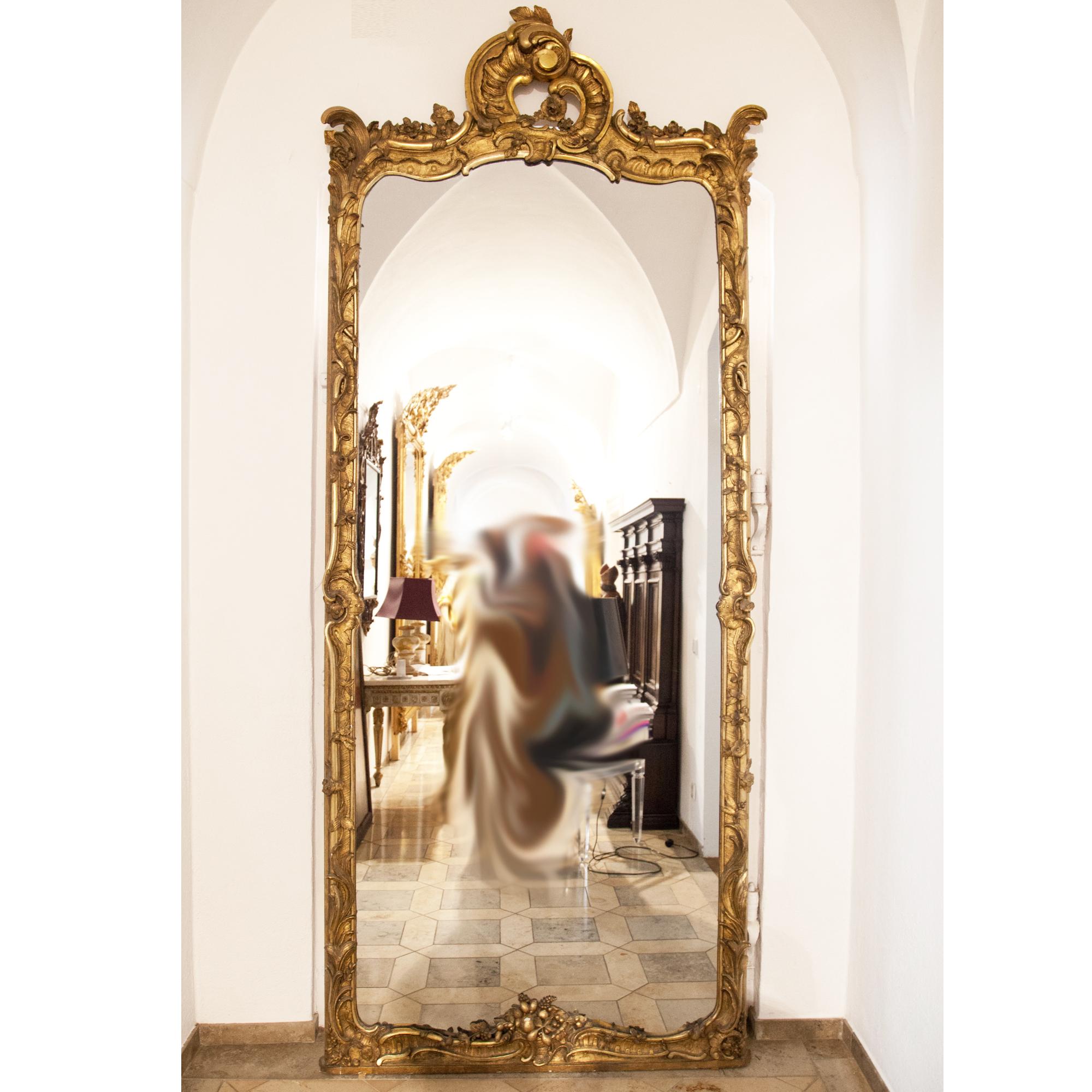 Long wall mirror in carved gold-patinated wooden frame with rocaille and fruit decorations.