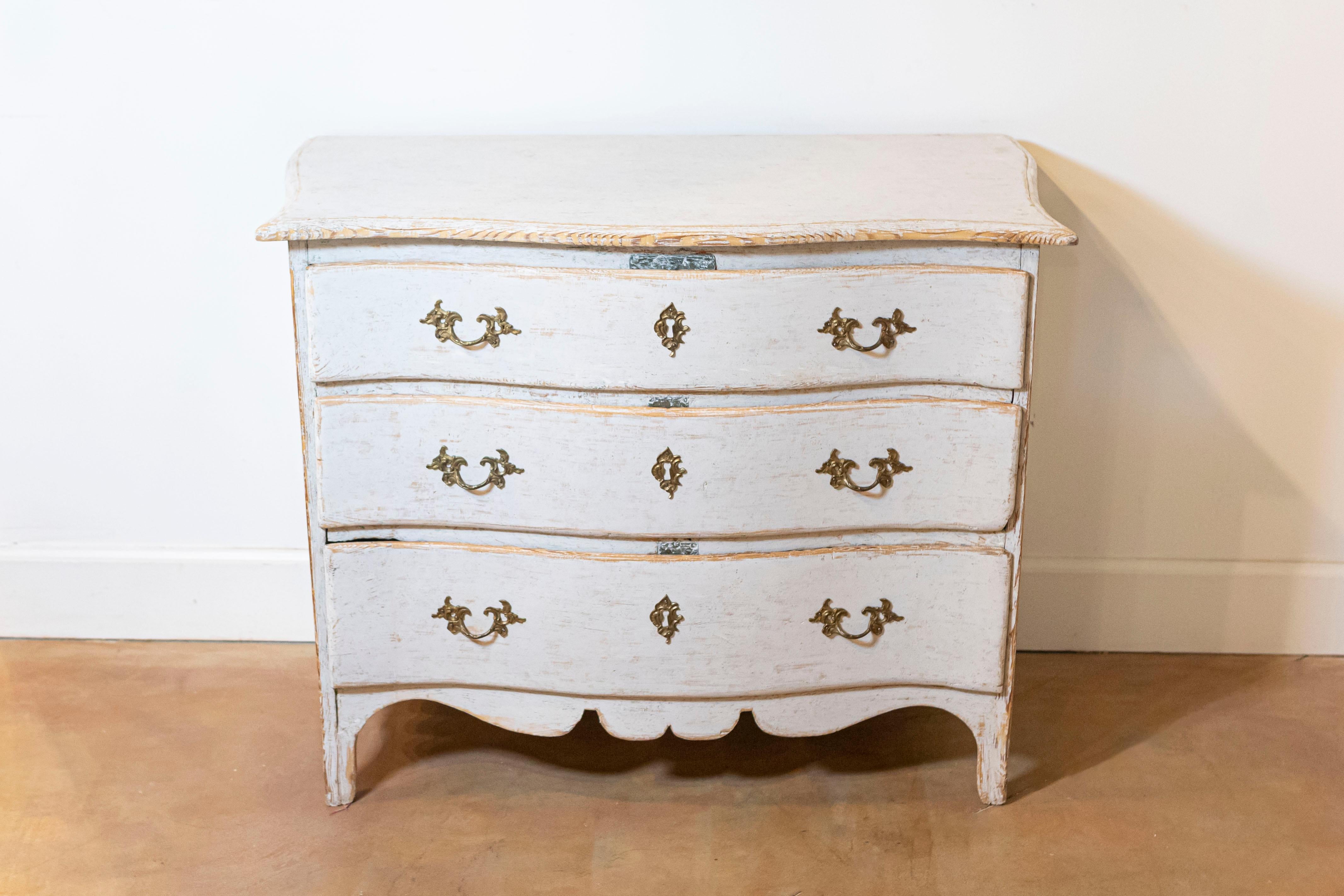 A Swedish Rococo period three-drawer commode from circa 1770 with light gray cream painted finish, carved skirt and serpentine front. This Swedish Rococo period three-drawer commode, dating back to circa 1770, is a magnificent example of the opulent