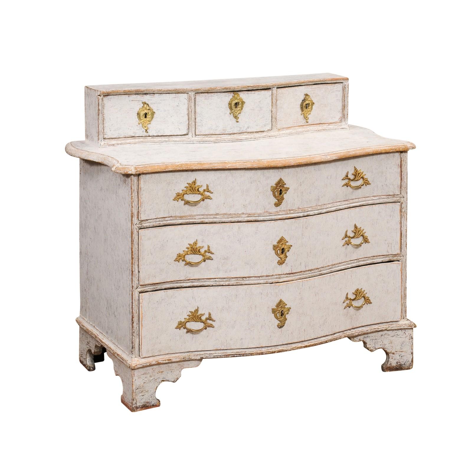 A Swedish Rococo period commode from circa 1760 with light Gustavian gray painted finish, raised shelf on the top, three drawers and bronze hardware. Immerse yourself in the grace and sophistication of the Swedish Rococo period with this enchanting