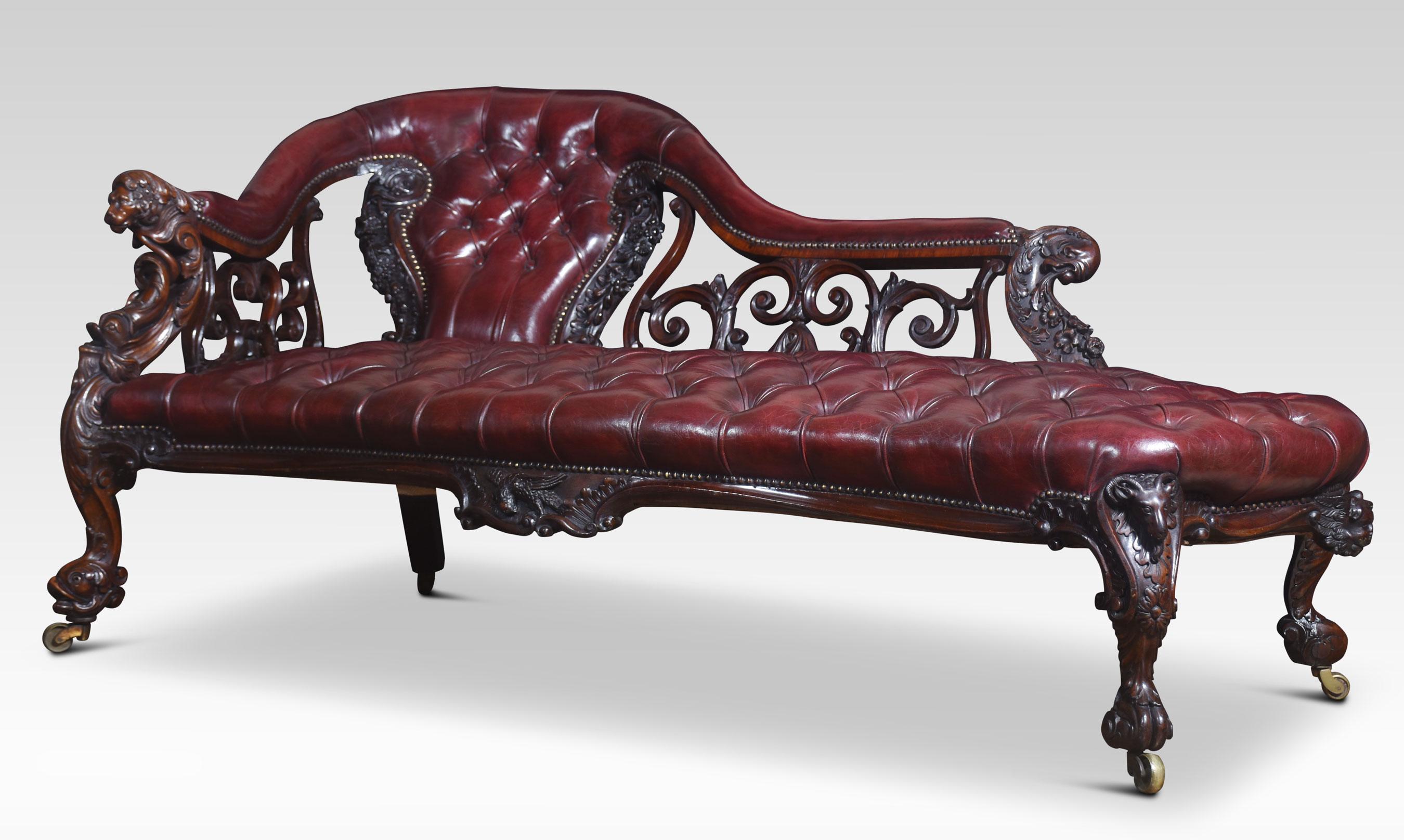 Rococo revival chaise longue, upholstered in burgundy hand-dyed deep buttoned leather. The carved and pierced back with scrolling decoration. To the arms carved with lion heads. All raised up on dolphin head carved feet terminating in brass