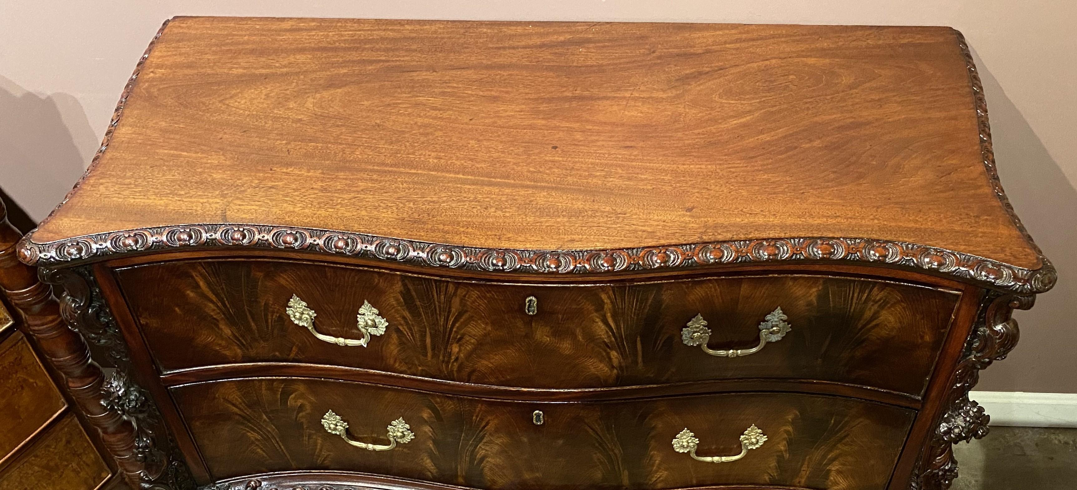 A spectacular Rococo Revival mahogany heavily carved serpentine two drawer commode, with a conforming top with carved border surmounting a case with two long drawers, each with foliate decorated pulls and bookmatched crotched mahogany veneers,