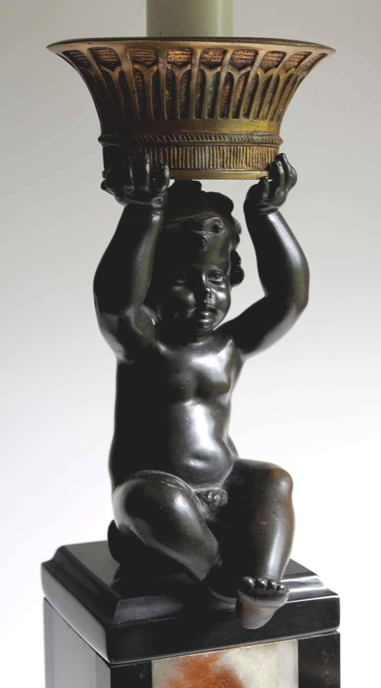 A black and white rectangular onyx base supports a finely cast bronze sculpture of a sitting putti upholding a bronze basket. Includes a matching unique black and white shade. Base is 5