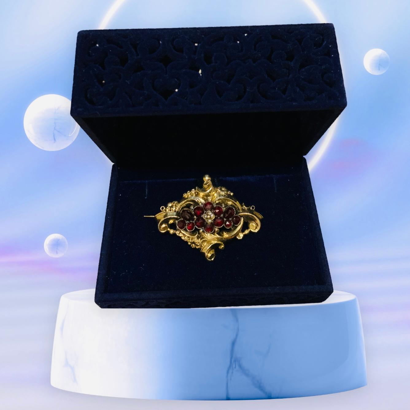 This is a 14K Yellow Gold Rococo Style Brooch. It depicts an oval brooch decorated with twelve old garnets and four seed pearls in the center. It is embellished by a 14K gold frame made of wide short C-scrolls, beads and flowers. Its weight is 2.9