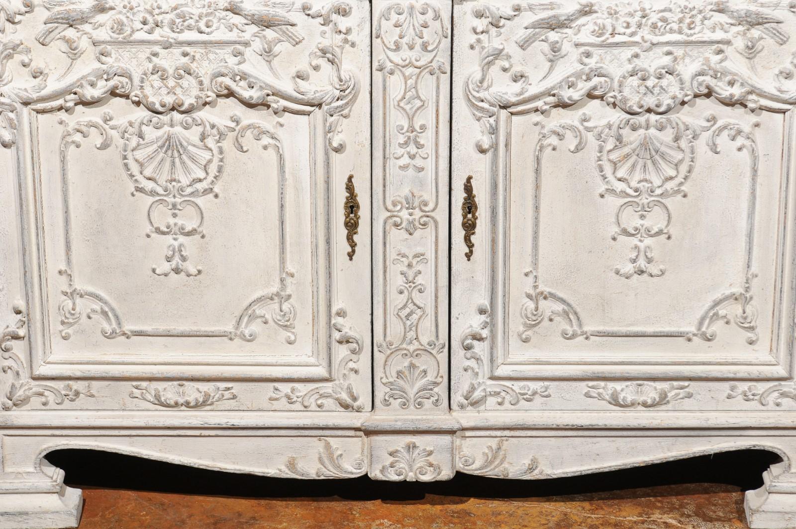 A Belgian Rococo style painted and carved wood buffet from the mid-19th century, with two drawers and two doors, richly carved décor of scrollwork, shell and bird motifs. Born in Belgium during the 1850s, this exquisite two-door painted buffet