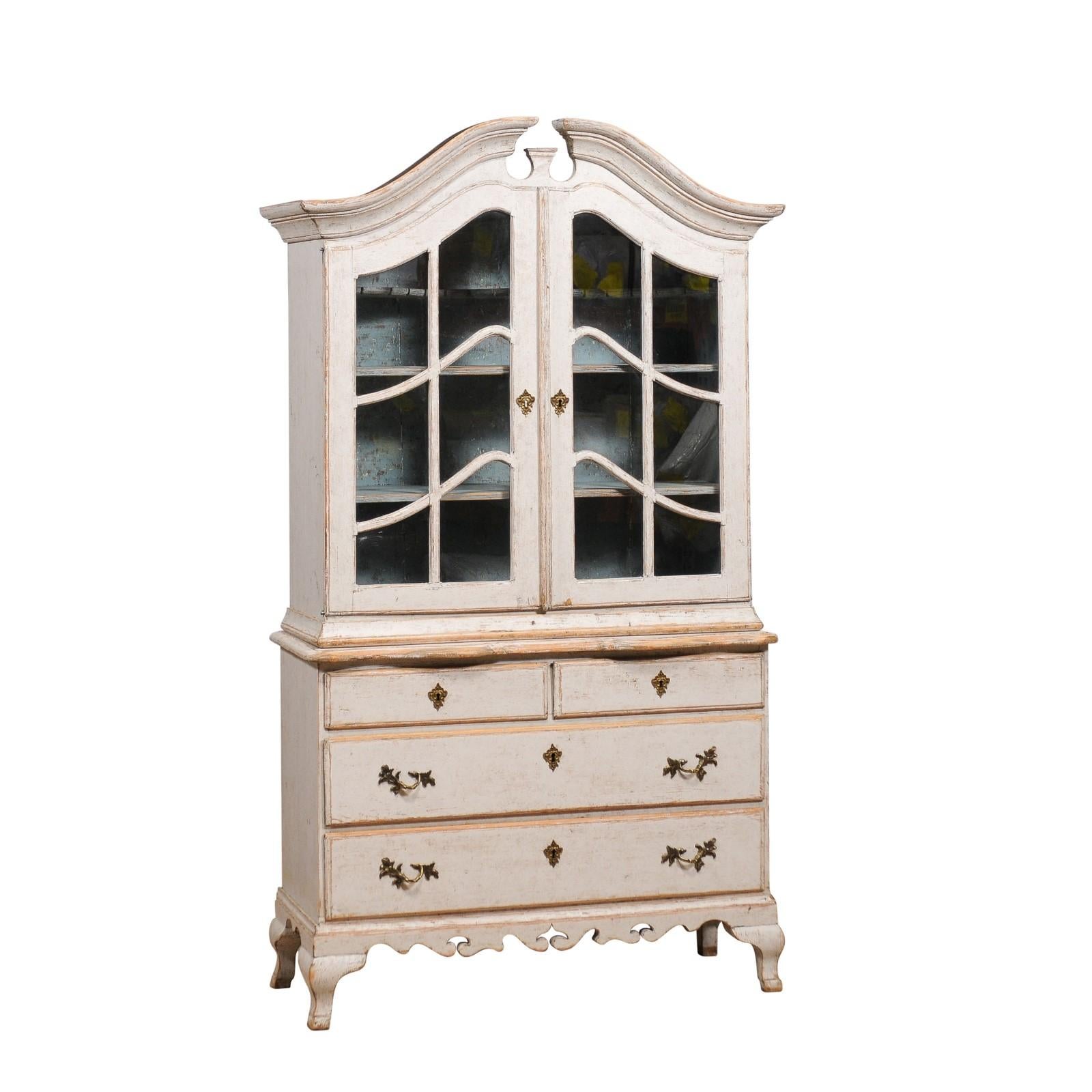 A Swedish Rococo style rich light grey painted vitrine cabinet from circa 1850 with bonnet top pediment, glass doors, four drawers, carved apron and curving feet. Emanate elegance with this Swedish Rococo-style vitrine cabinet from circa 1850, a