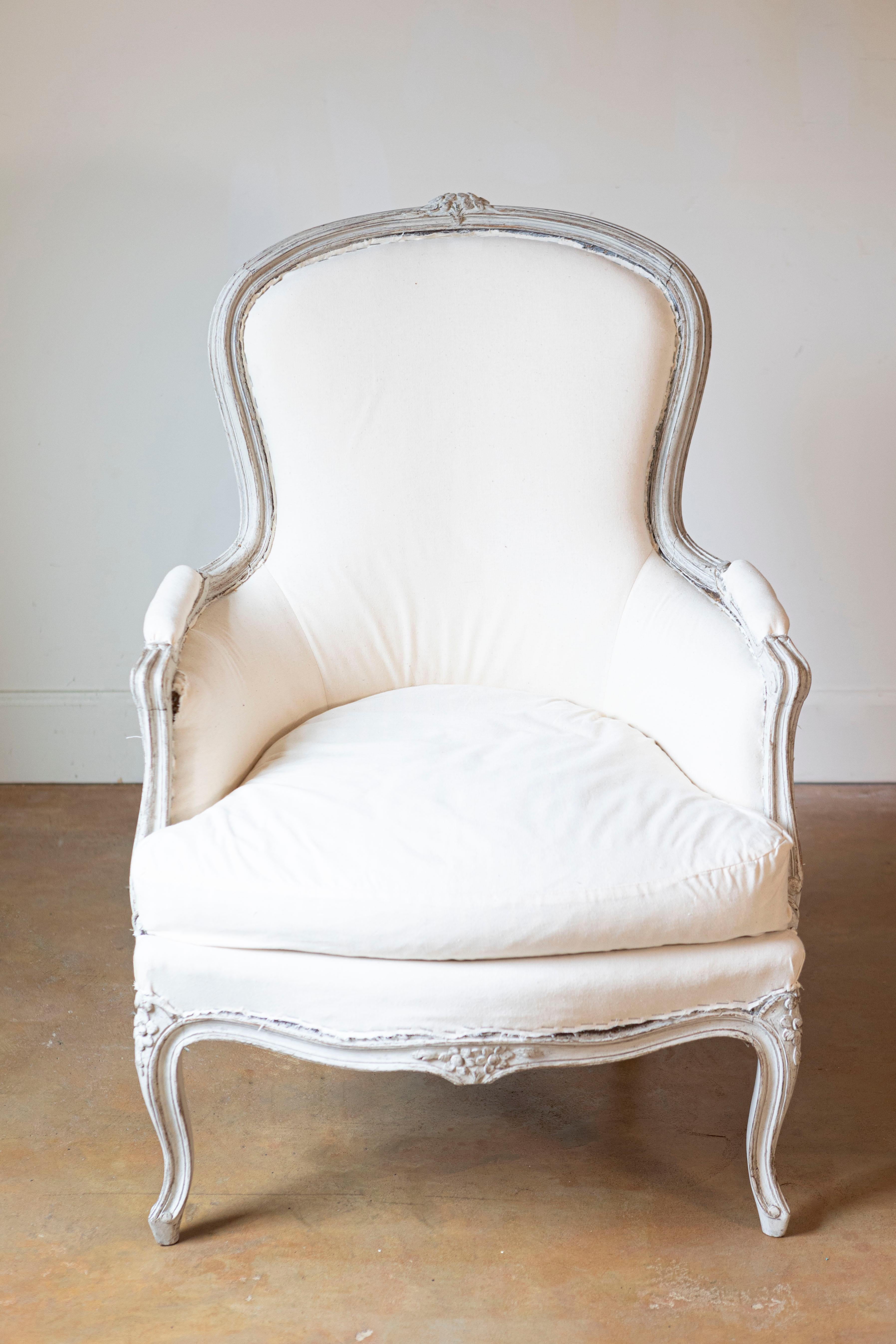 Ein schwedischer, klassischer, hellgrau lackierter Bergère-Stuhl im Rokoko-Stil aus der Zeit um 1890 mit geschnitztem Blumendekor, Cabriole-Beinen und gepolsterter Sitzfläche. Mit seinen zarten floralen Motiven, die anmutig in den Kamm, die Knie und