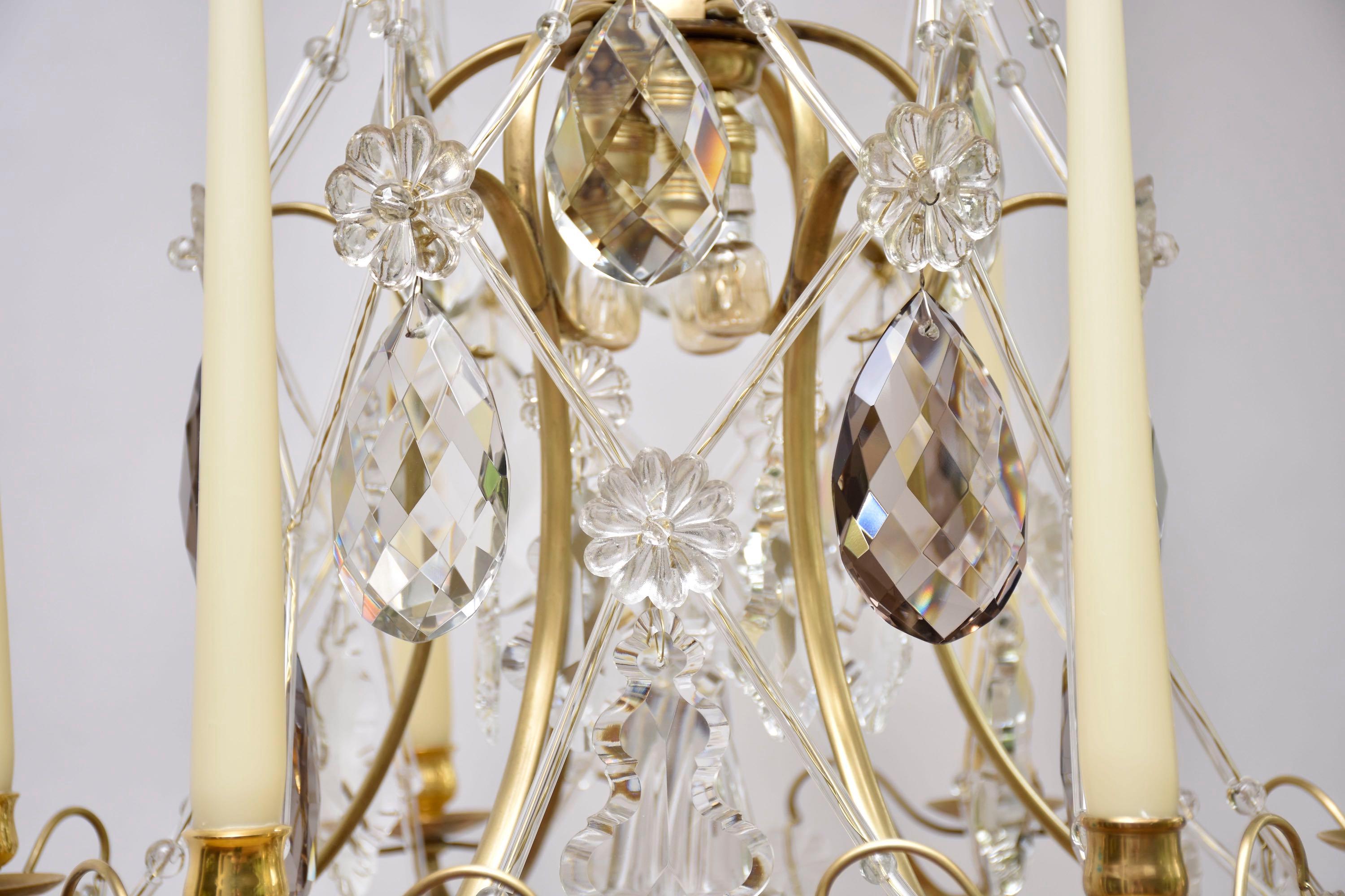 Ein eleganter nordeuropäischer Rokoko-Kronleuchter mit 3 kleinen Innenleuchten und 6 Kerzenarmen.
Verziert mit mehreren Pendeloques in klarem und zartfarbigem böhmischem Kristall, Blumenrosetten und Sternen. Sehr schön und dekorativ sind die