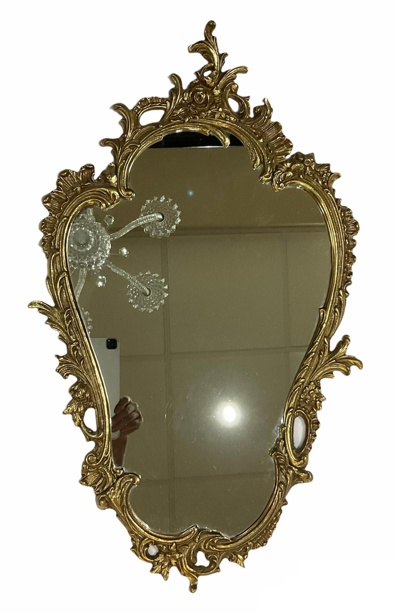 This is a Rococo Style gilt wall console mirror. It is kind of an asymmetric up side down pear shaped mirror. It is adorned with large scrolls of acanthus leaves and “rocailles” in its frame. There is also some branches of flowers interwined with