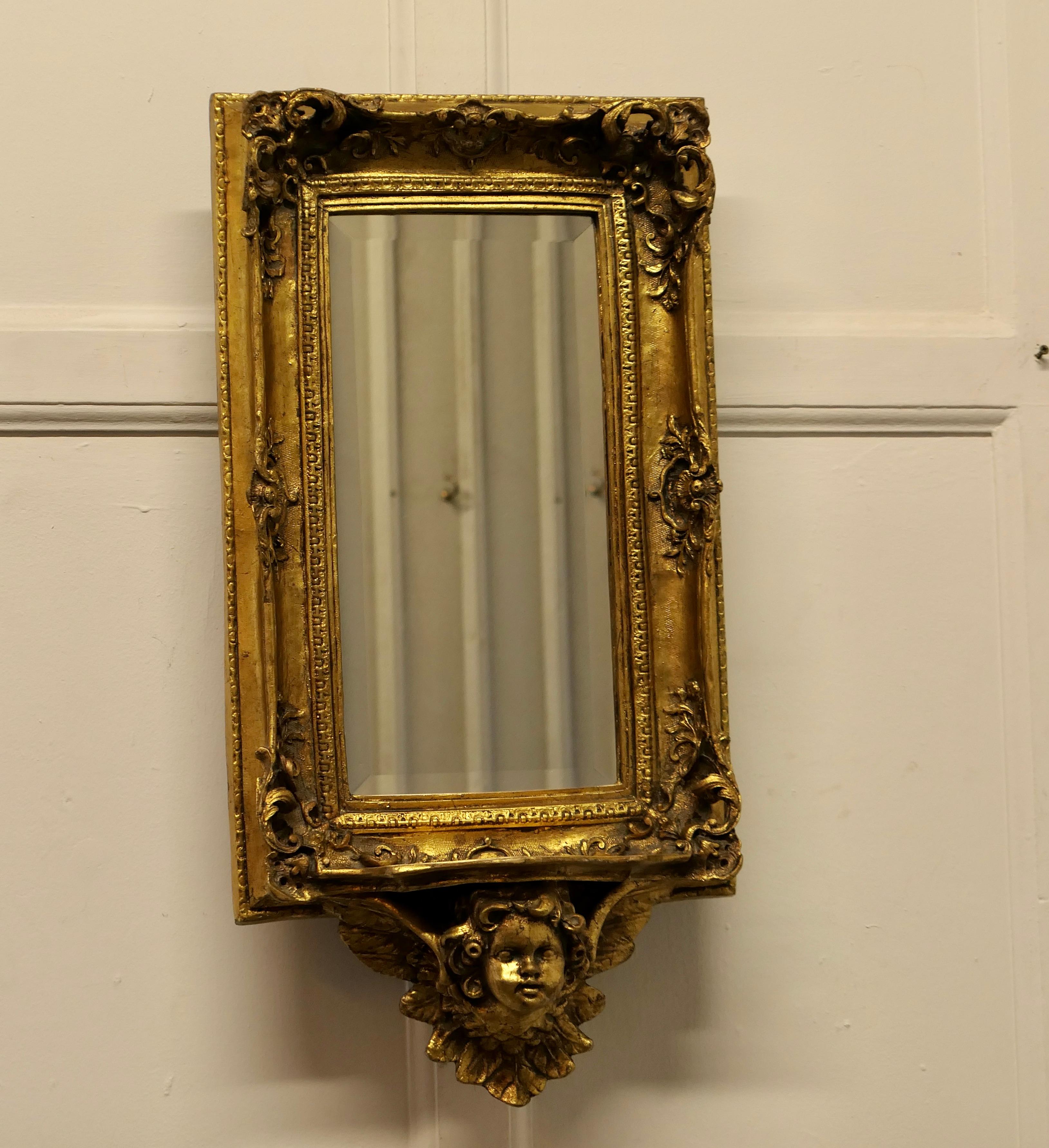 Rococo Style gilt wall mirror with Putti and Shelf Bracket.

The mirror has an exquisite gilt Frame in the Rococo Style, it is rectangular in shape and has the face of a putti angel at the bottom supporting a small shelf 
In good age darkened