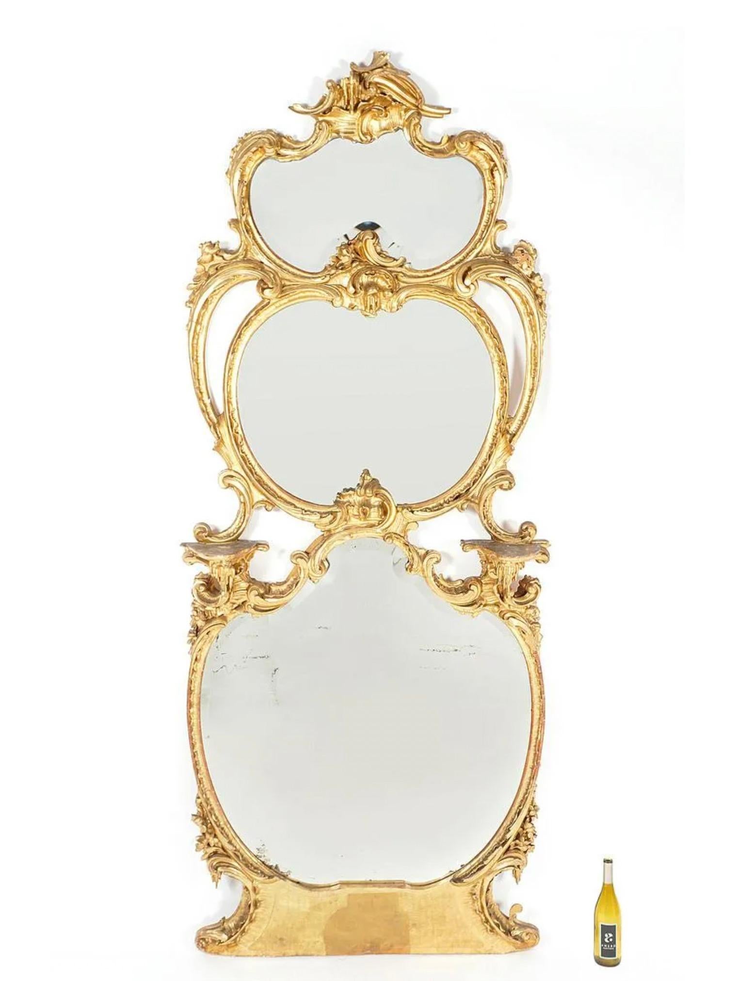Large Italian rococo style gilt wood wall mirror, frame with foliate scroll and shell motifs, two candle shelves. Three shaped mirror panels.
 