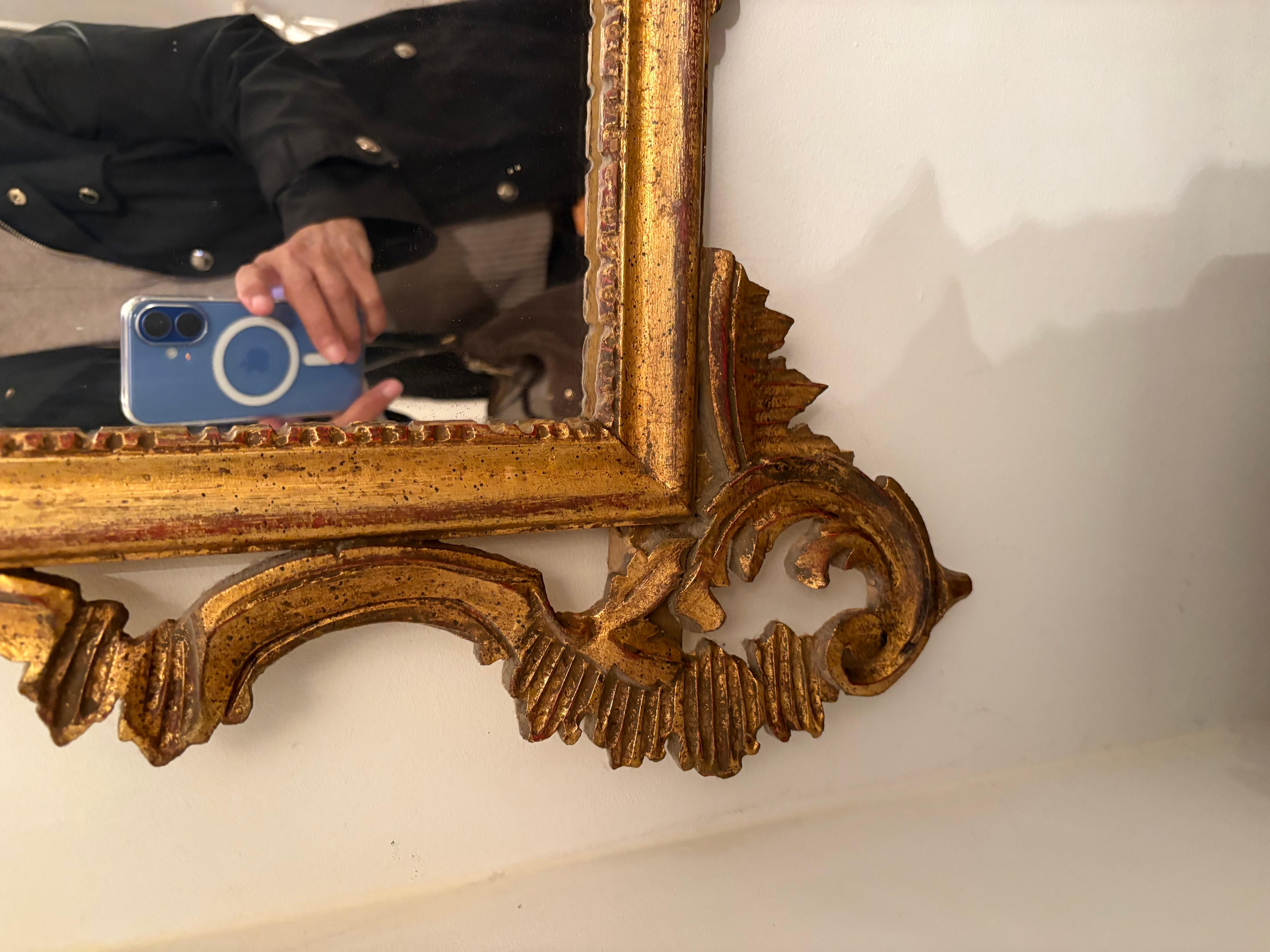 Grande specchio da parete in legno dorato intagliato in stile French Rococo attribuito a Labarge della metà del XX secolo. Lo specchio presenta una cornice molto decorata con una voluta floreale intagliata a mano e un grande frontone ad
