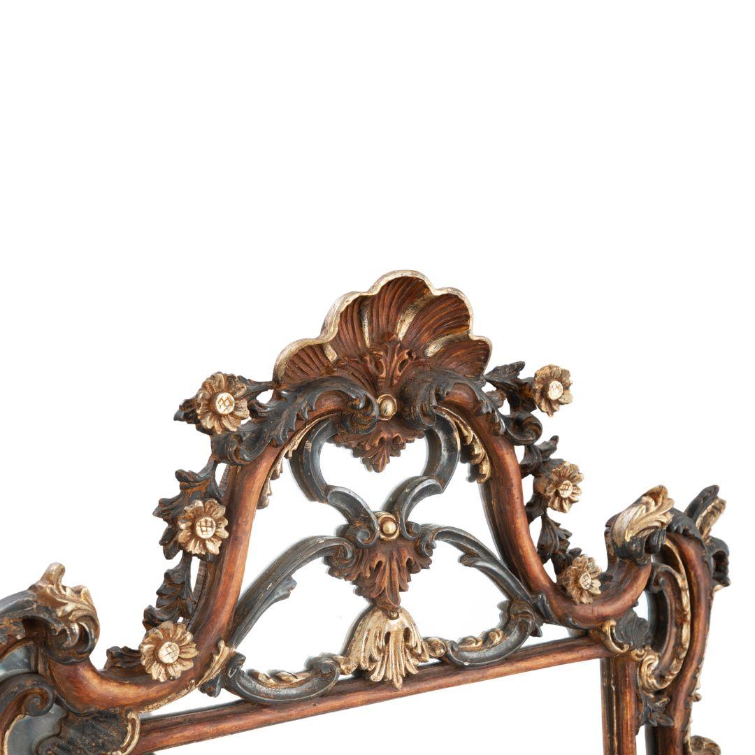 Dieser Wandspiegel im Rokoko-Stil hat einen polychromen Rahmen auf einem Kreidegrund mit Teilvergoldung. Der rechteckige Rahmen hat ein dynamisches, wellenförmiges Design und gipfelt in einer gewölbten Oberseite, die mit einem gekrönten Muschelmotiv