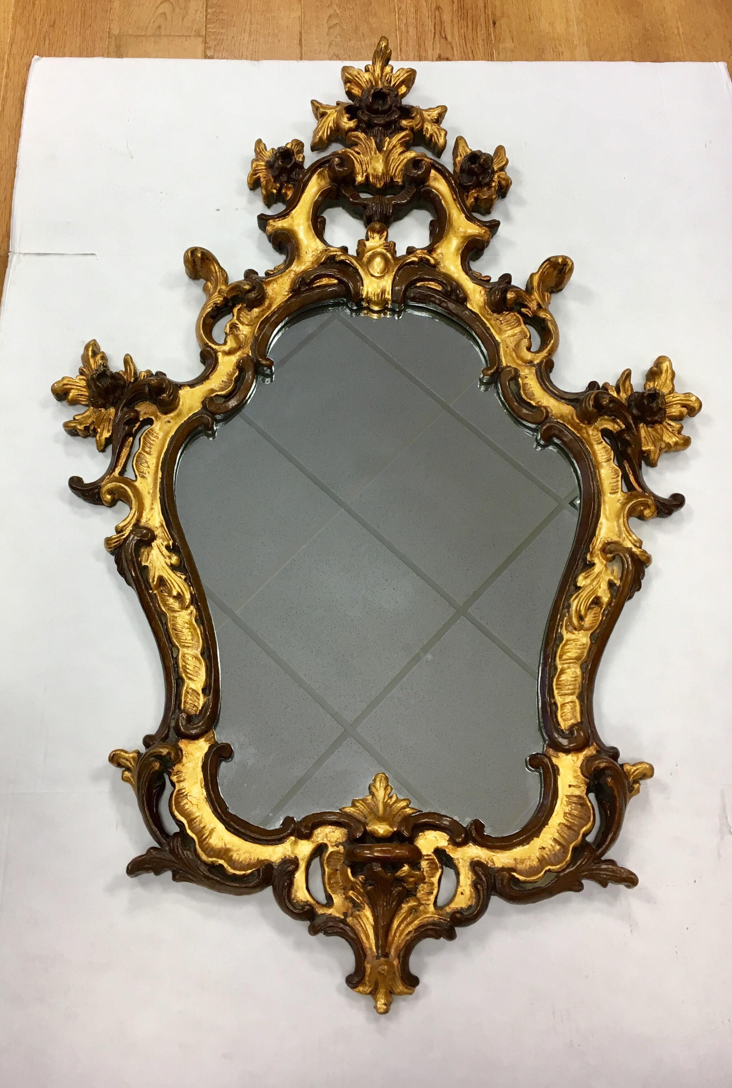 Beautifully hand carved Italian Rococo style giltwood shield wall mirror with elegant design features that include scrolls and acanthus leaves. The mirror has a hand carved lime wood frame that was smoothed with dark gesso and gilt with gold leaf