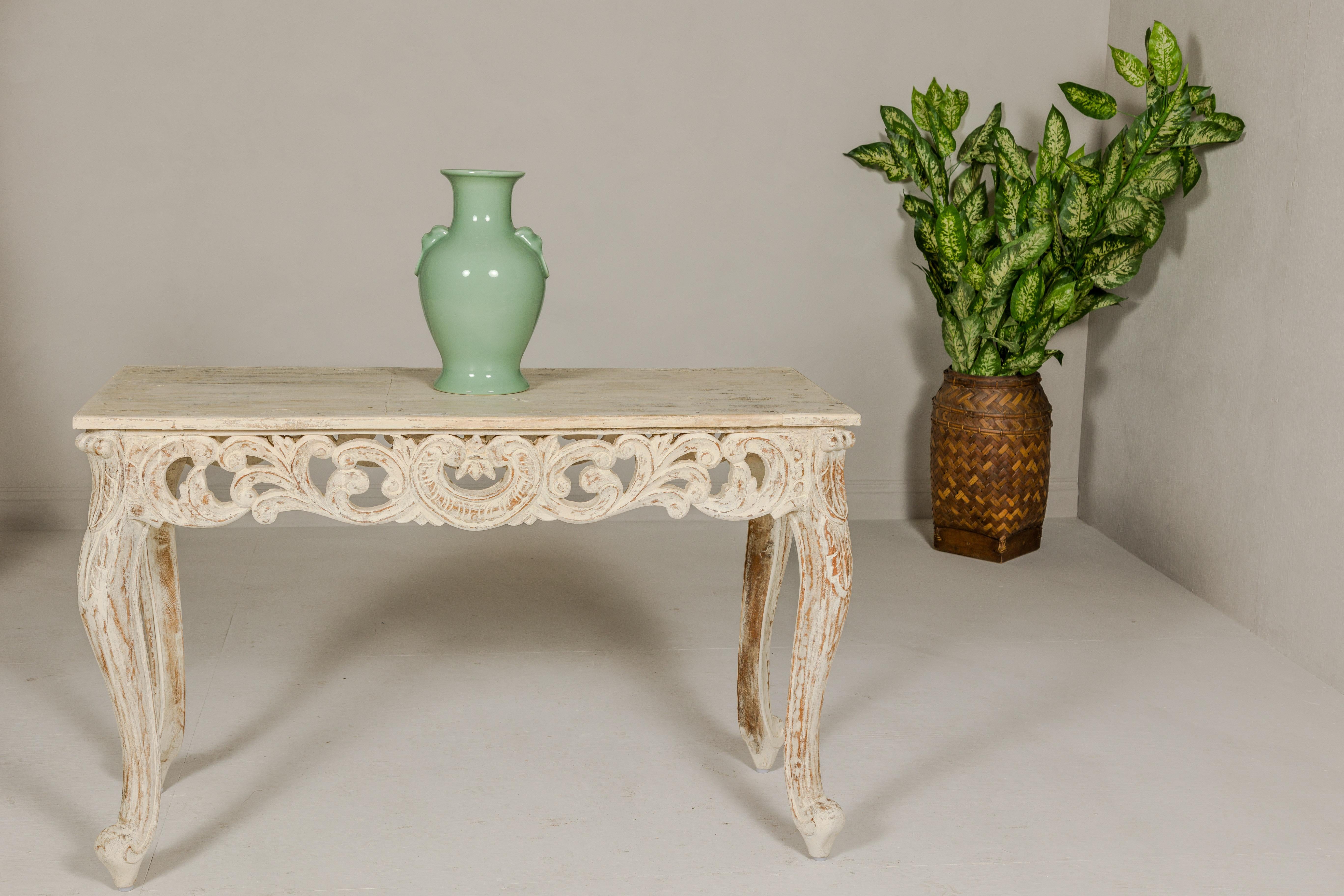 A Rococo style console table with distressed painted finish, carved apron, cabriole legs and scrolling feet. We have two available. Introduce a touch of timeless elegance to your home with this exquisite Rococo style console table, featuring a